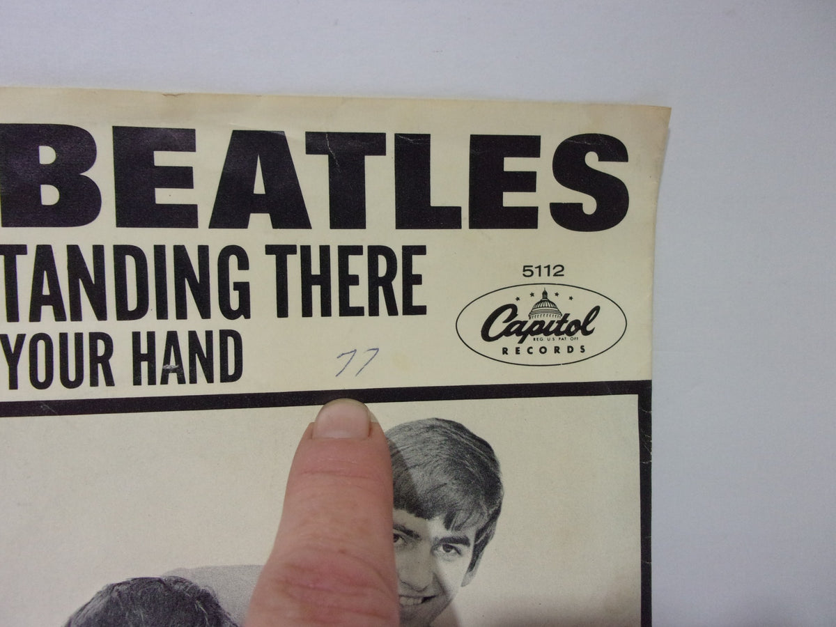 The Beatles: I Want To Hold Your Hand Capitol Records 5112 45RPM single cover with a finger pointing to a handwritten note, highlighting its collectible nature.
