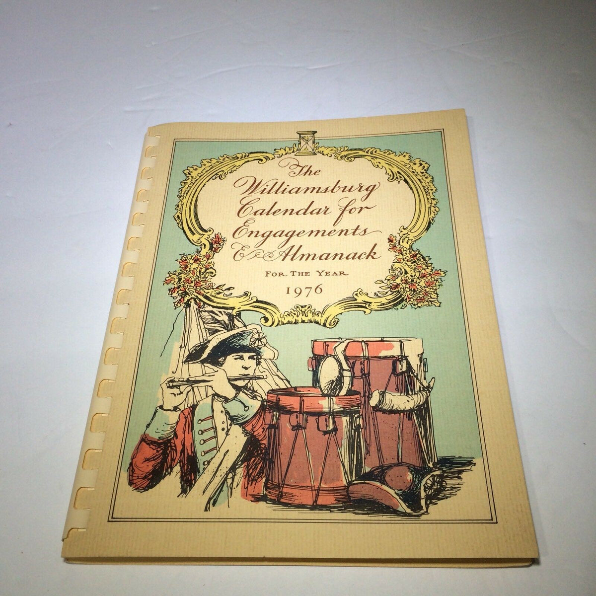 Front view of the Vintage 1976 Williamsburg Calendar & Almanack with an eye-catching design featuring a colonial musician and drums, highlighting the artistic representation of the 1970s vintage era.