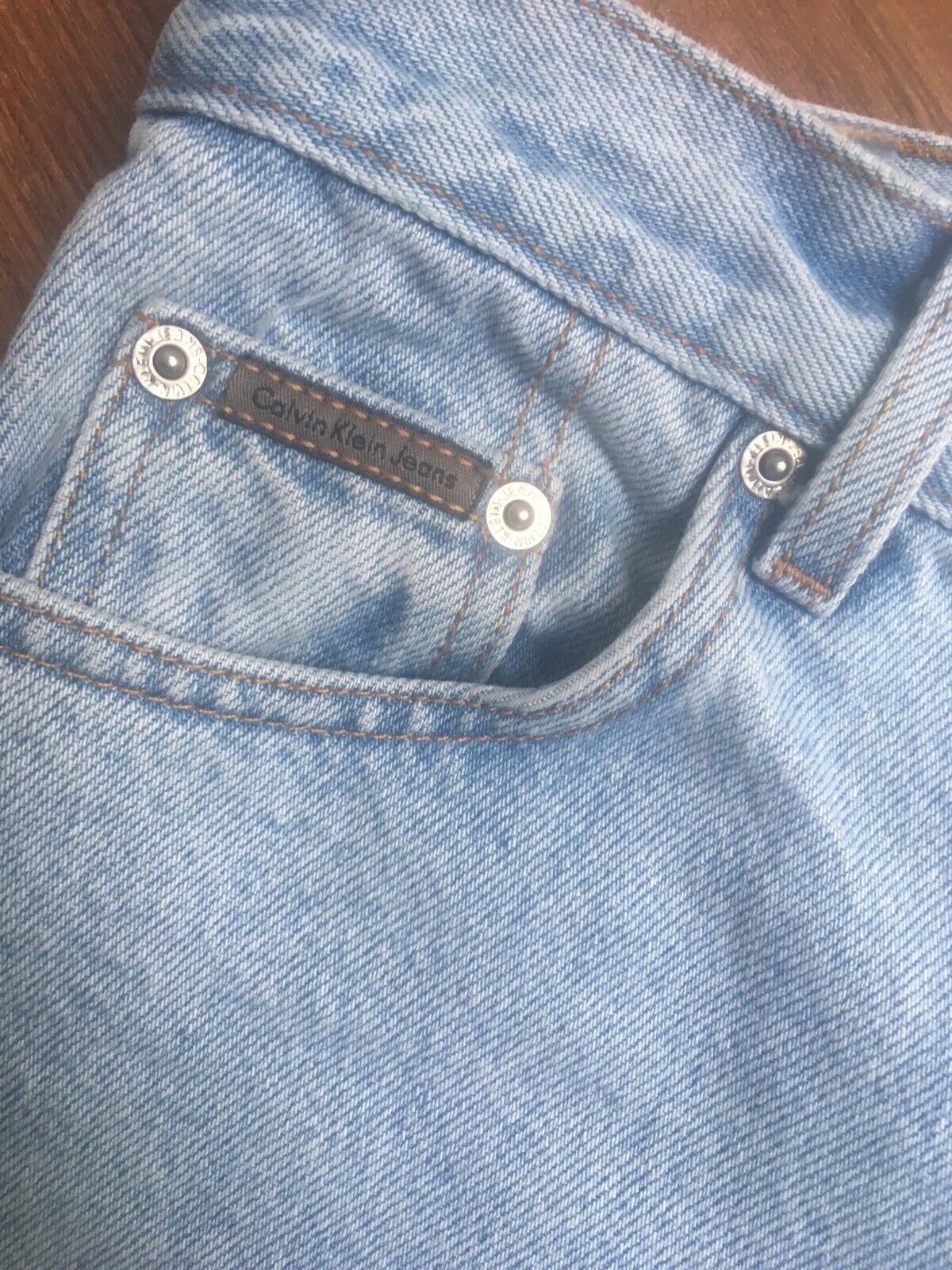 Close-up of Vintage 90s Calvin Klein High Rise Mom Jeans Light Blue Denim showing the signature Calvin Klein jeans tag on the waistband for authenticity.