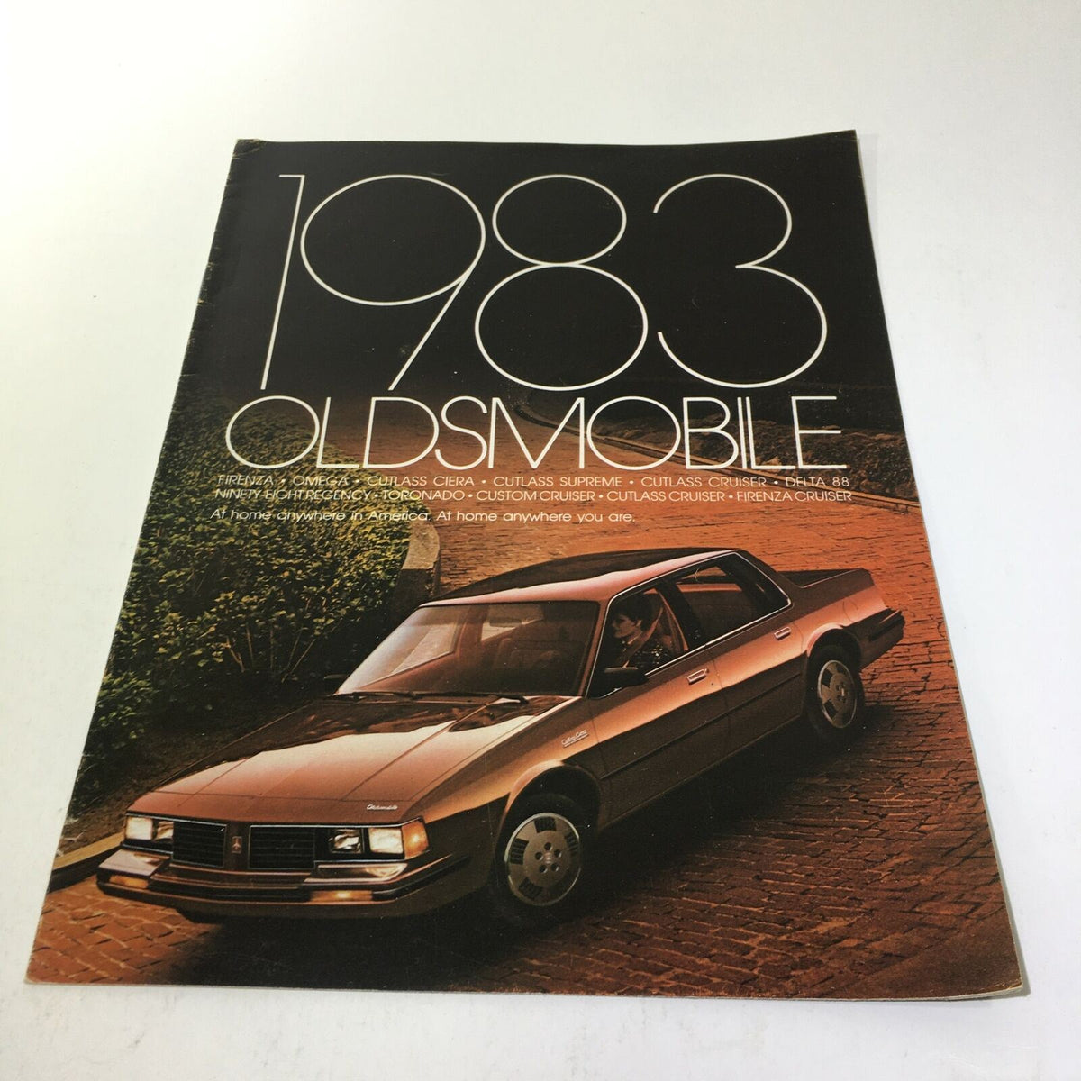 Cover of the 1983 Oldsmobile Firenza 'S' Coupe and 4-Door Sedan brochure featuring a brown car parked on a scenic driveway.