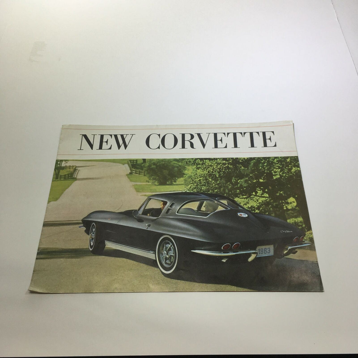 1963 New Corvette Sting Ray Sport Coupe Sale Brochure showcasing a sleek black Corvette design on a scenic road.