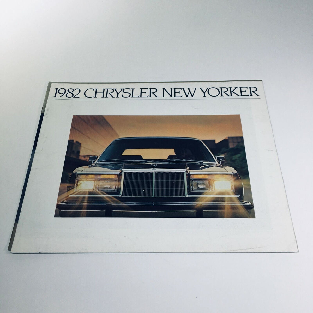 Cover of the 1982 Chrysler New Yorker V-8 OHV 6-cyl OHV 8/81 Car Sale Brochure showcasing the front of the vehicle against a scenic backdrop.