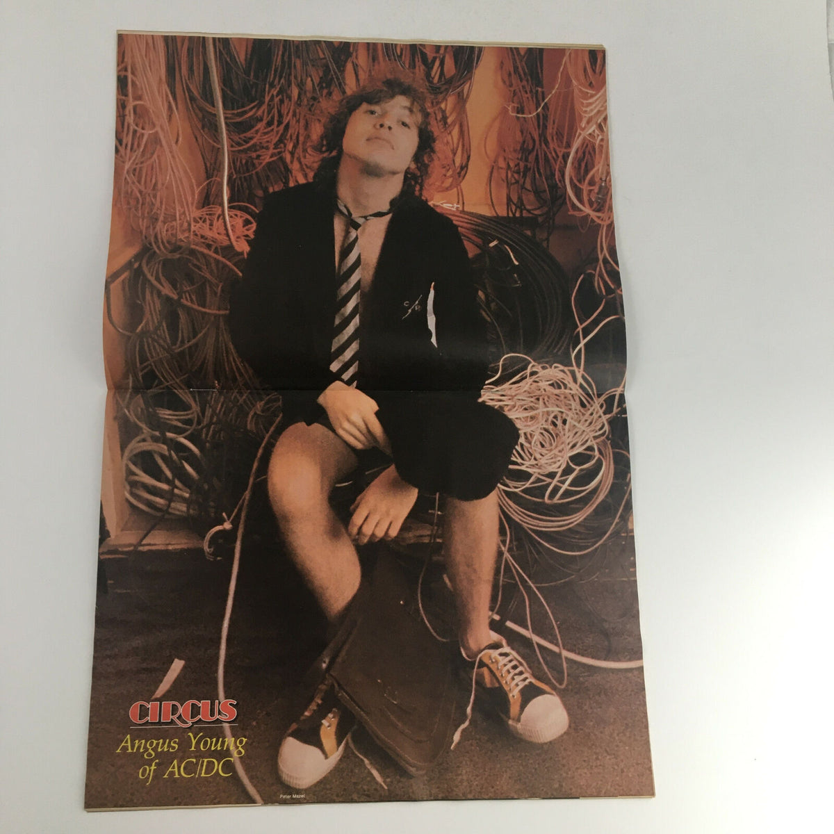 Vintage poster featured in Circus Magazine November 27 1979, showcasing Angus Young of AC/DC, sitting amidst tangled wires, embodying the rock spirit of the late 1970s. A collectible item from a historic music publication.