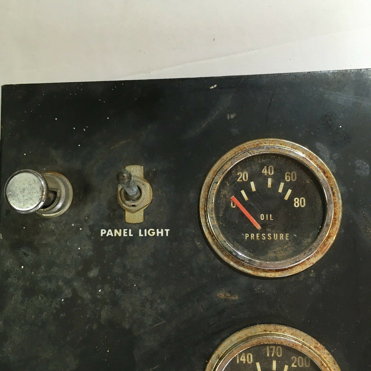 Close-up view of a panel featuring a pressure gauge for oil and a panel light switch. Part of a Temperature Water, Oil, Amps, Meter, Gauge Triple Auto Panel, designed for monitoring performance metrics in machinery.