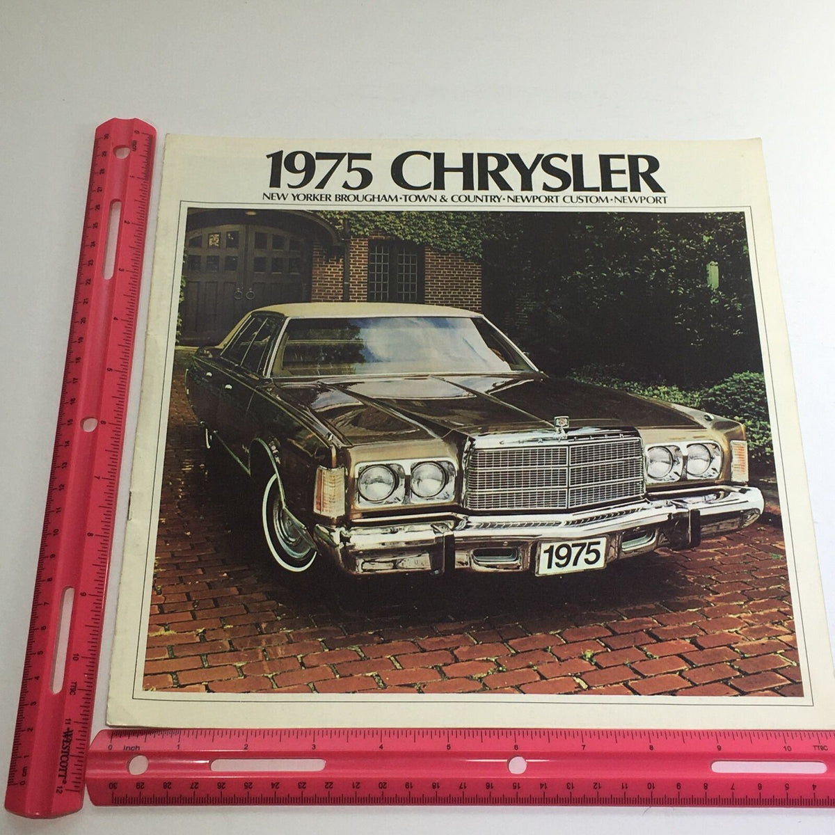 1975 Chrysler New Yorker Brougham Dealership Brochure Cover featuring a classic car parked on a brick driveway with elegant architecture in the background.