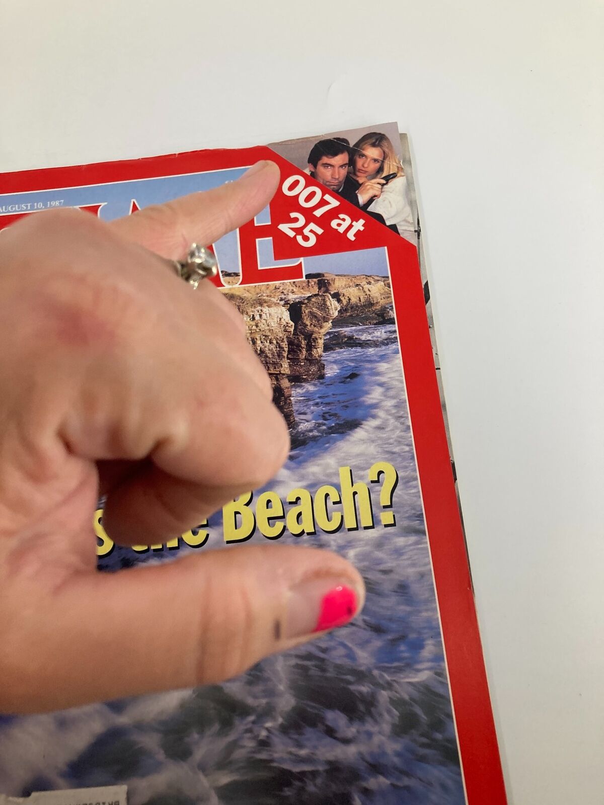 Hand pointing to the corner of VTG Time Magazine August 10 1987, showcasing the '007 at 25' feature and the oceanic imagery on the cover.