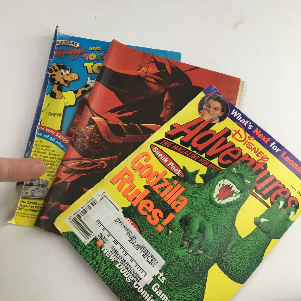 Three vintage Disney Adventures magazines stacked together, prominently displaying the June 1998 issue with Godzilla on the cover and a feature on Leonardo DiCaprio.