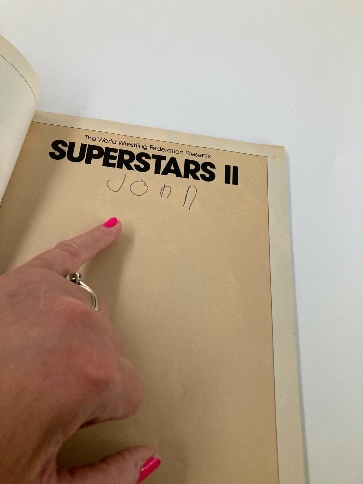 The World Wrestling Federation Presents Superstars II 1987 displaying a handwritten name 'John' inside the book with a pointing finger.