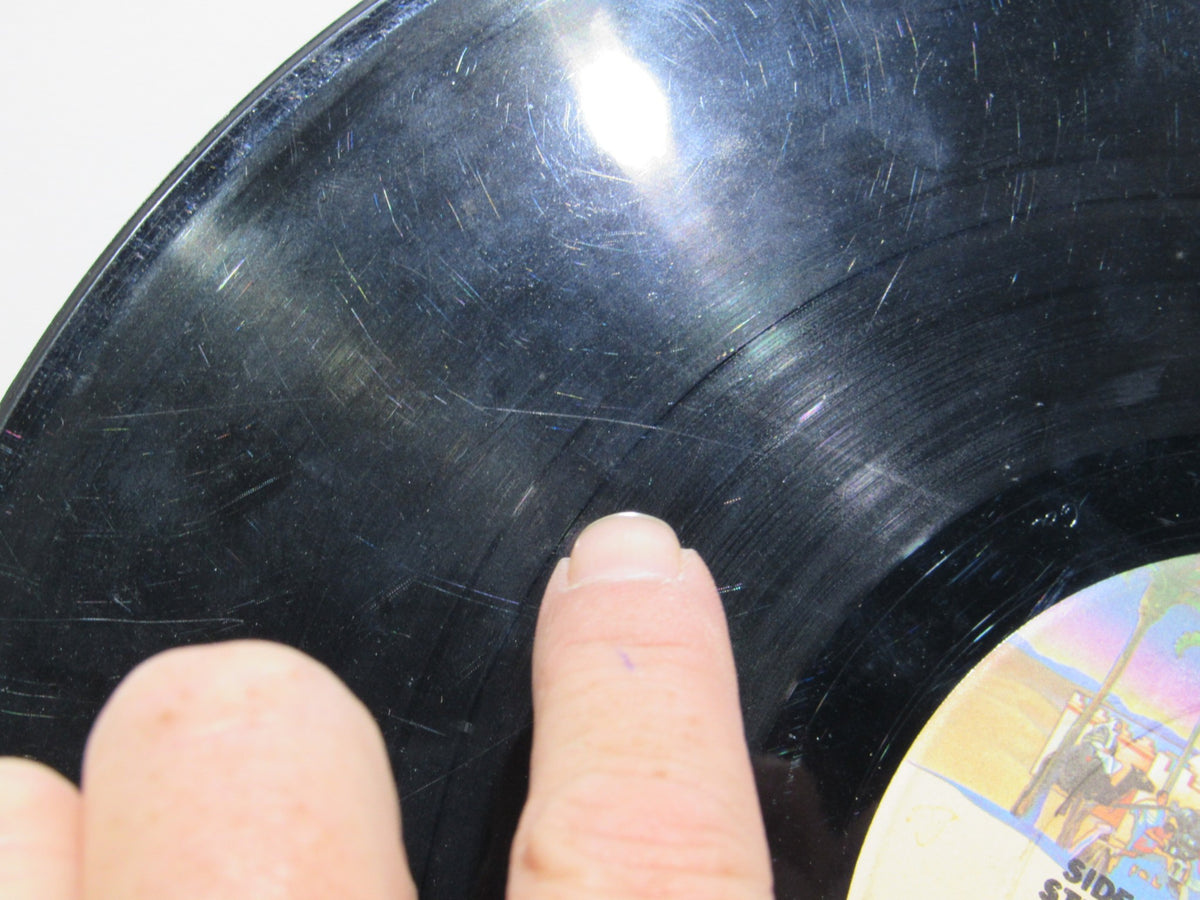 A hand pointing at scratches on the surface of 'Donna Summer: Greatest Hits on the Radio LP NBLP 27191' vinyl, indicating used condition.