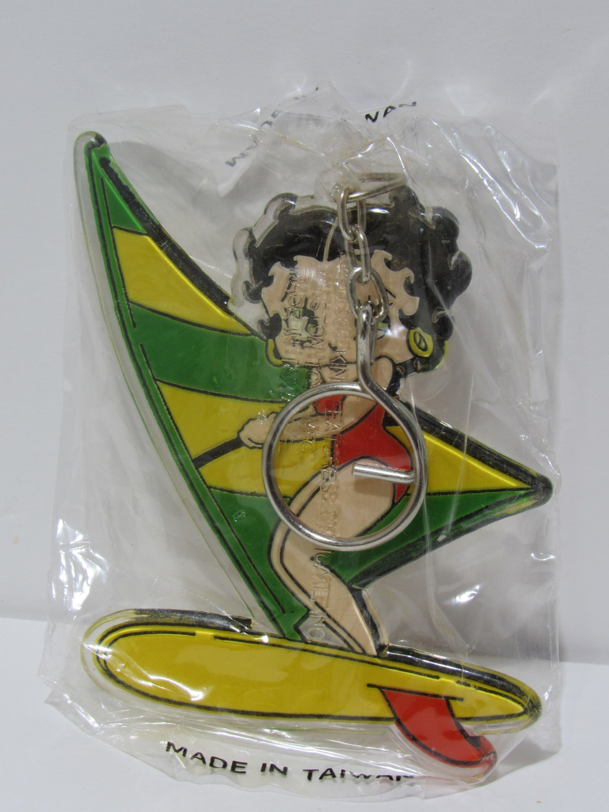 1985 Rare Vintage Surfing Betty Boop Key Chain, showcasing Betty Boop holding a surfboard and wearing a red swimsuit with a colorful sail, preserved in original packaging.