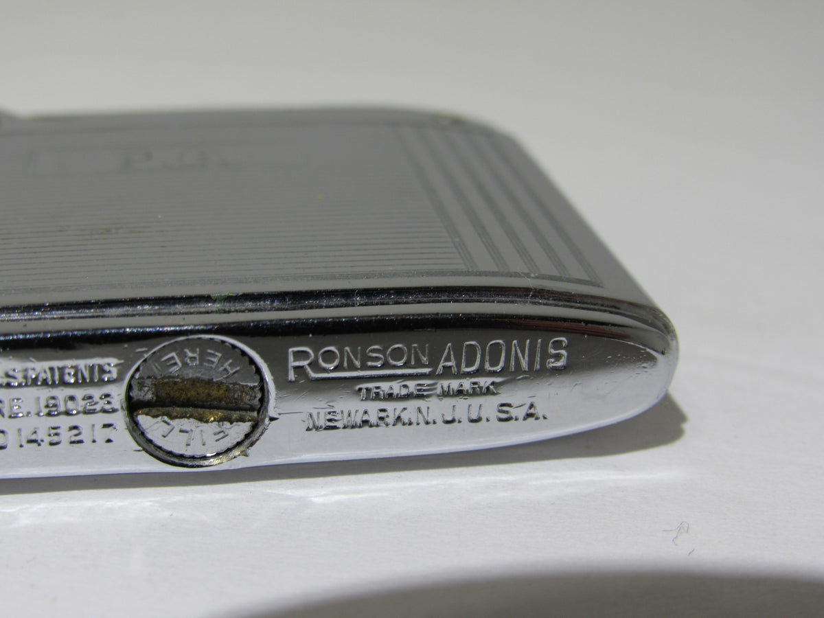 Close-up of the engraving on Vintage Ronson Adonis Chrome Striped Lighter #145217, showing the Ronson Adonis trademark.