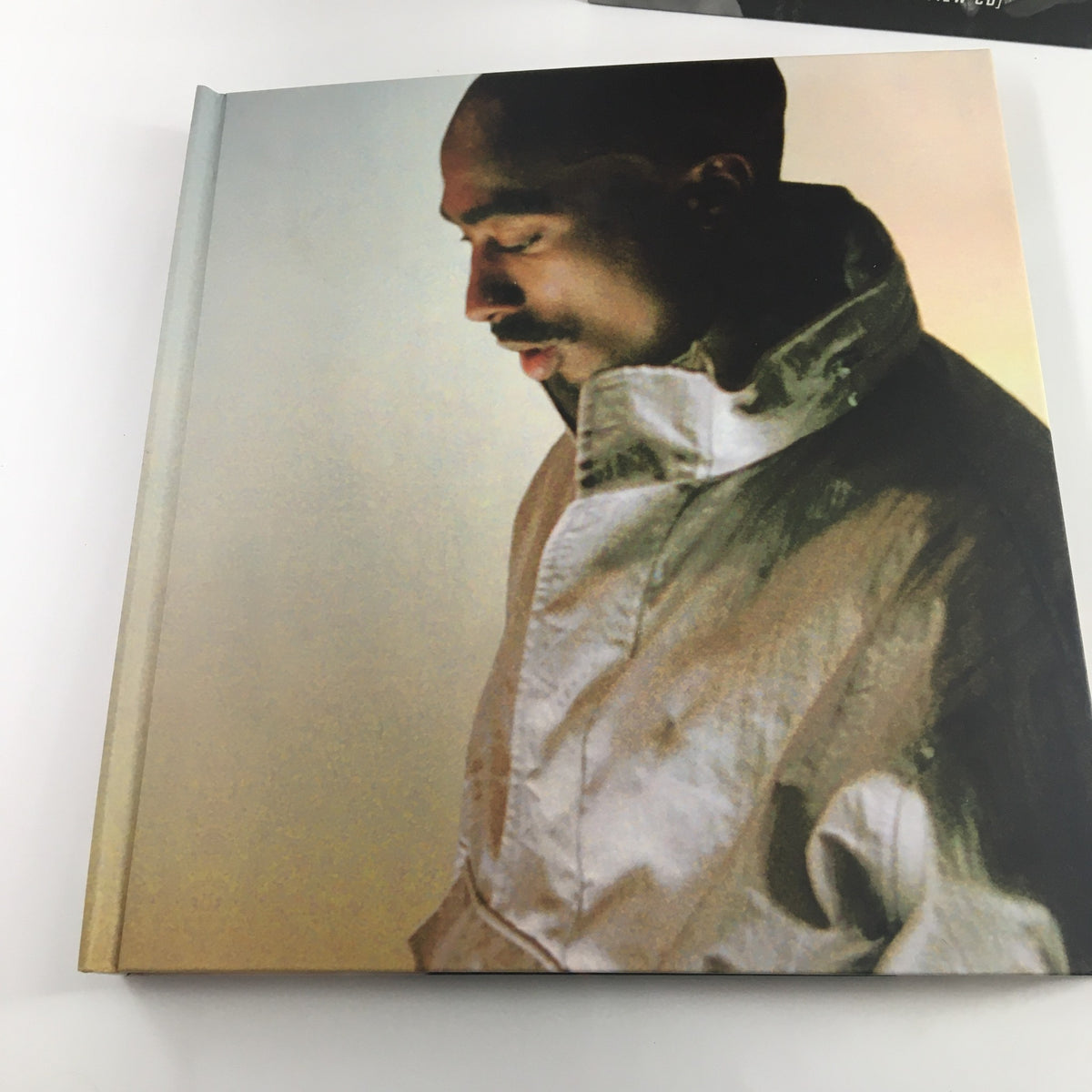 Close-up of the Tupac Shakur Legacy book showing an image of Tupac with a contemplative expression, dressed in a light-colored jacket.