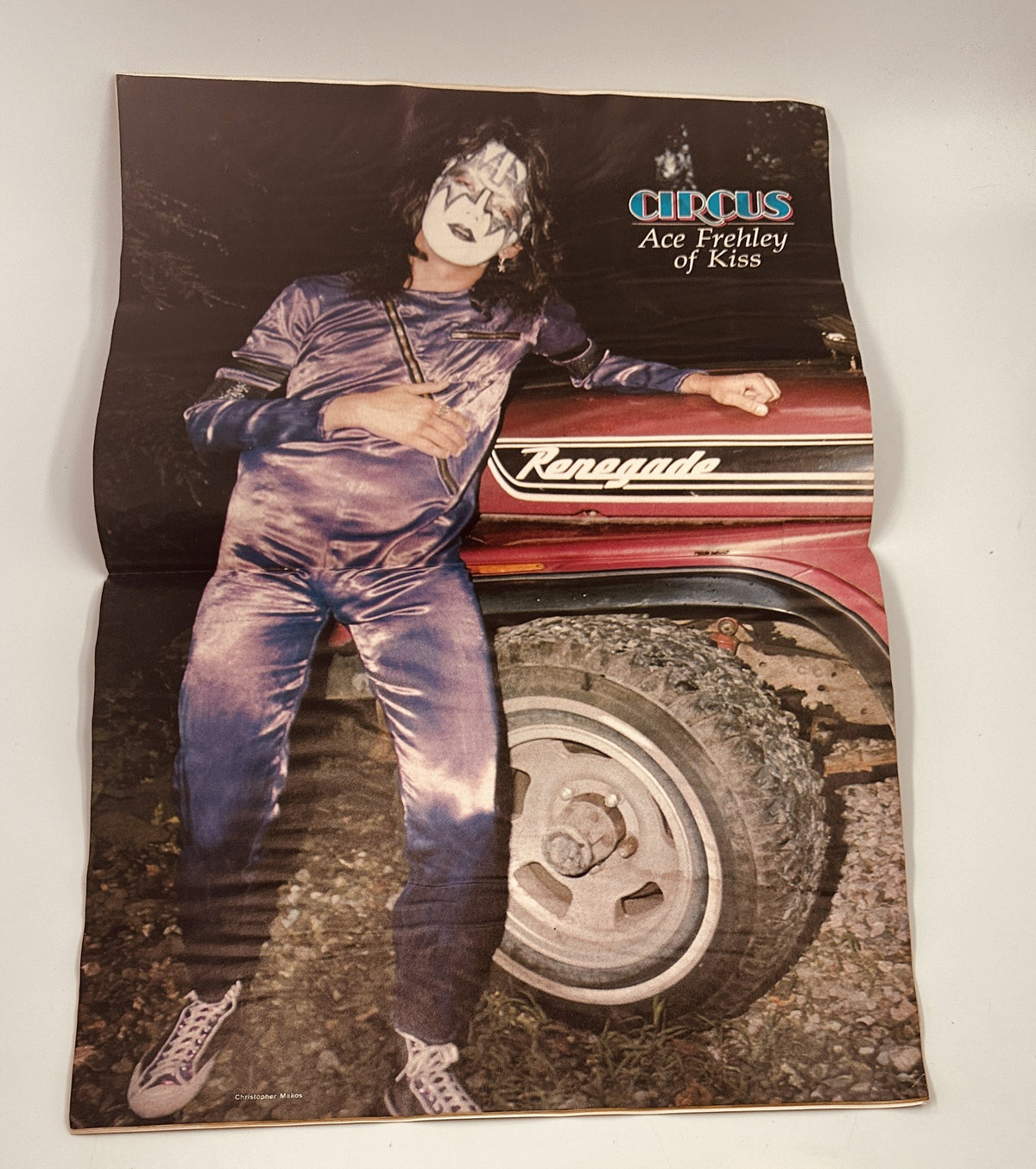 Promotional image of Ace Frehley from Kiss, sporting a signature look beside a vehicle; featured in Circus Magazine April 27, 1978.