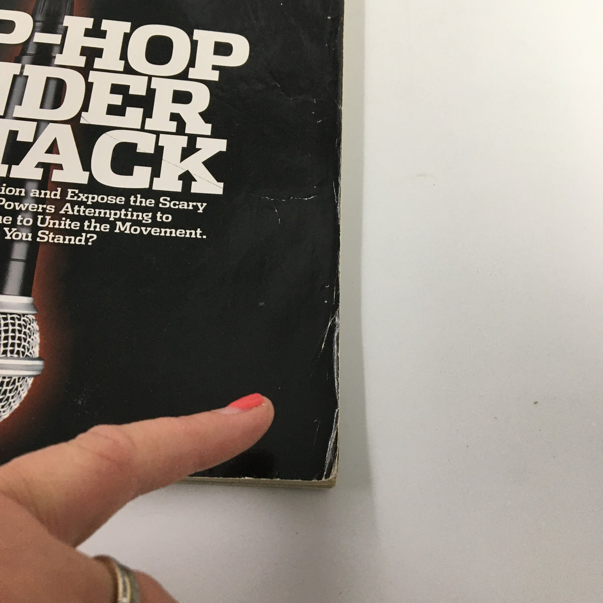 Side view of The Source Magazine March 2003 No. 162 showcasing the text 'HIP-HOP UNDER ATTACK' with a hand pointing towards it, indicating wear and condition.
