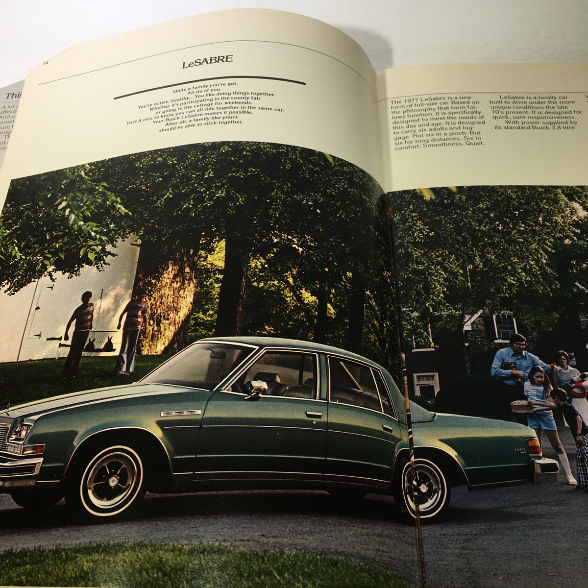 Interior image from the 1977 Buick Buyer's Guide showcasing the LeSabre model, with a family depicted around the car, illustrating the vehicle's appeal for family use and comfort.