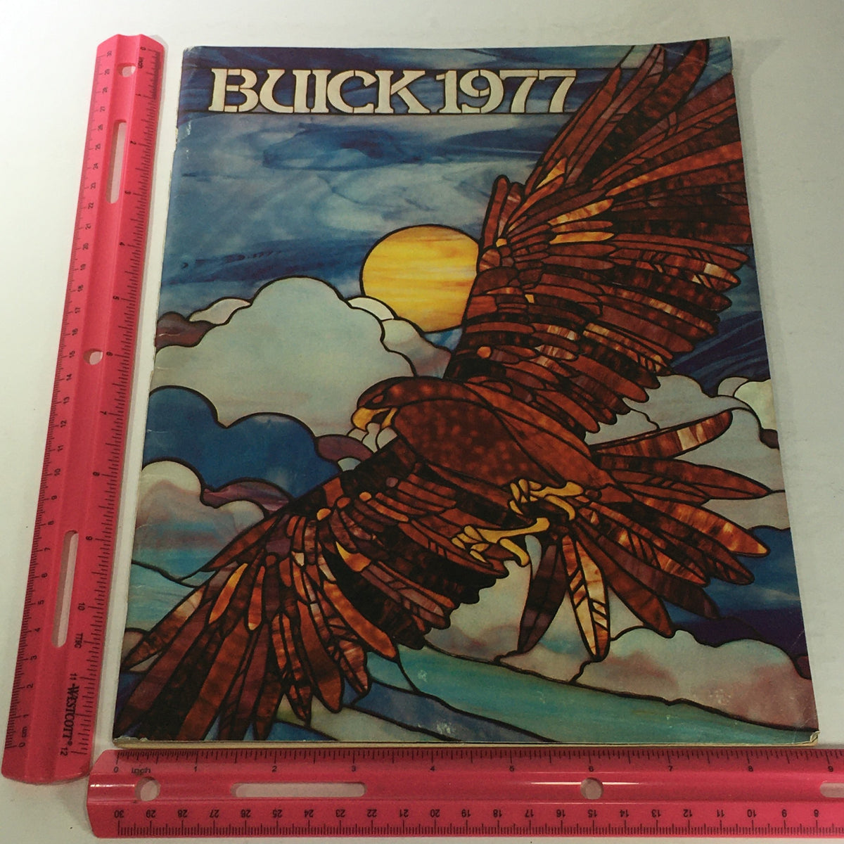 Front cover of the 1977 Buick Buyer's Guide with a colorful stained glass artwork of an eagle against a sunset backdrop, representing the iconic models of the year.