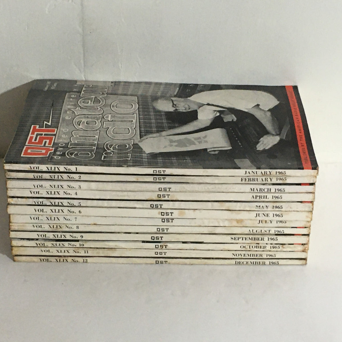 Lot of 12 Complete January to December 1965 QST Amateur Radio magazines stacked, showcasing Volume 49 with visible issue numbers and a vintage cover design.