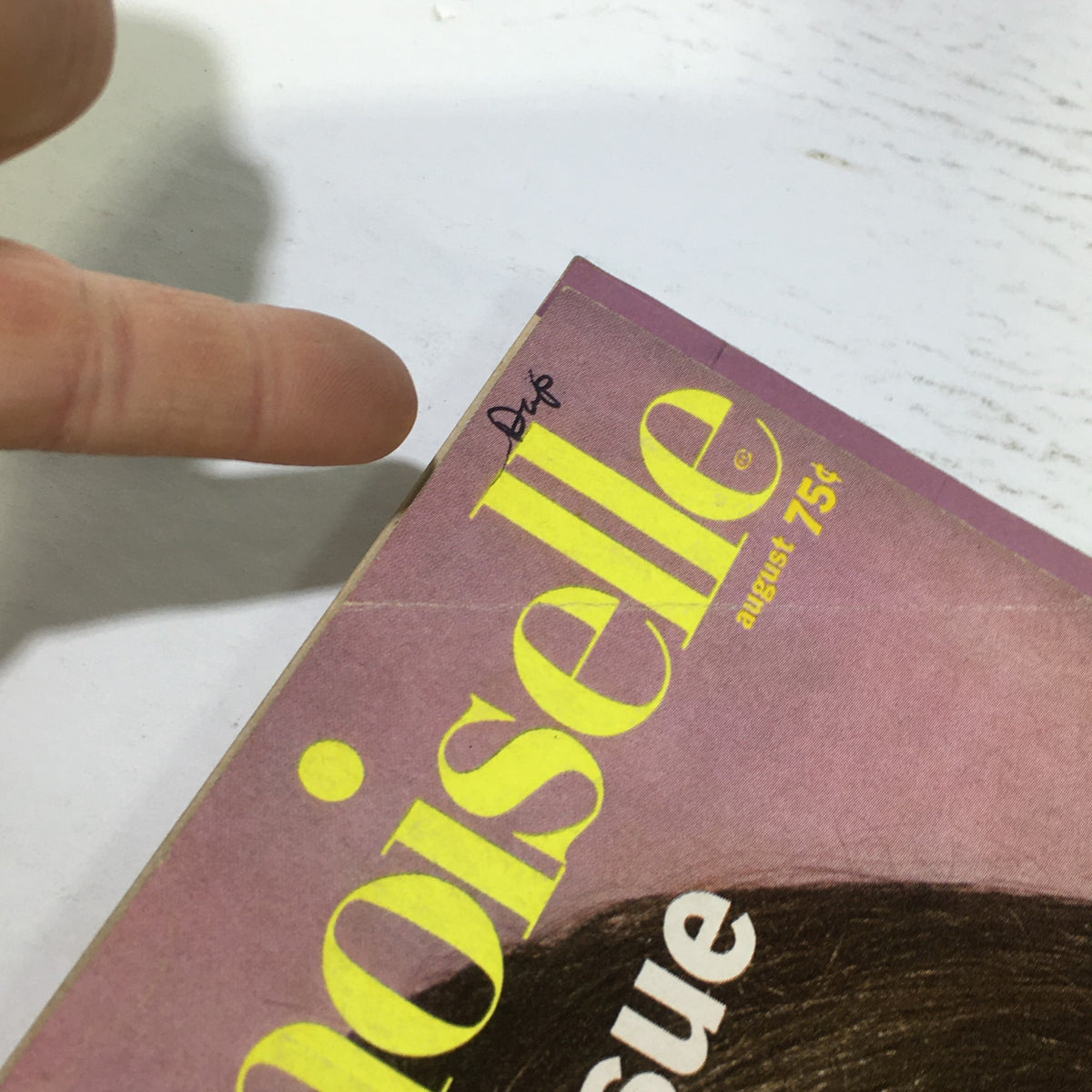 Close-up of the corner of the VTG Mademoiselle Magazine: August 1967 - Retro The College Issue, highlighting a handwritten date and the magazine's vibrant cover design with bold yellow letters.