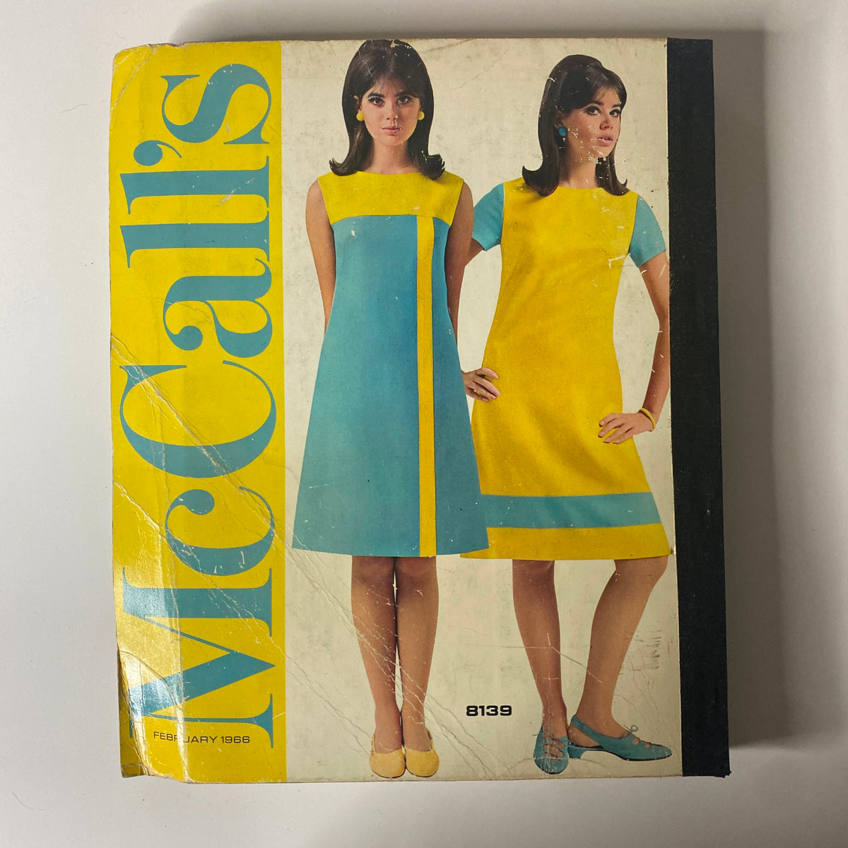 1966 February McCall's Designers' Collection Catalog cover featuring stylish women's dresses in blue and yellow colors. The image captures the essence of mid-1960s fashion, ideal for home sewing enthusiasts.