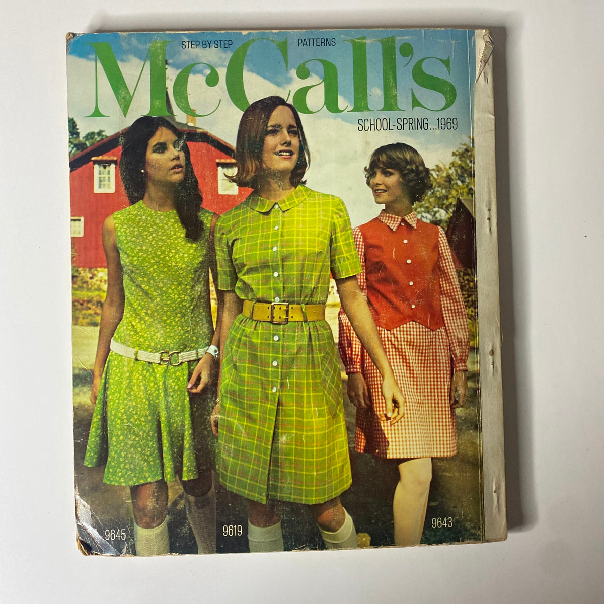 1969 McCall's School Spring Huge Store Retail Counter Catalog cover featuring three girls in vibrant dresses with a rustic red barn backdrop, representing classic 1960s youth fashion, perfect for sewing and vintage fashion collectors.