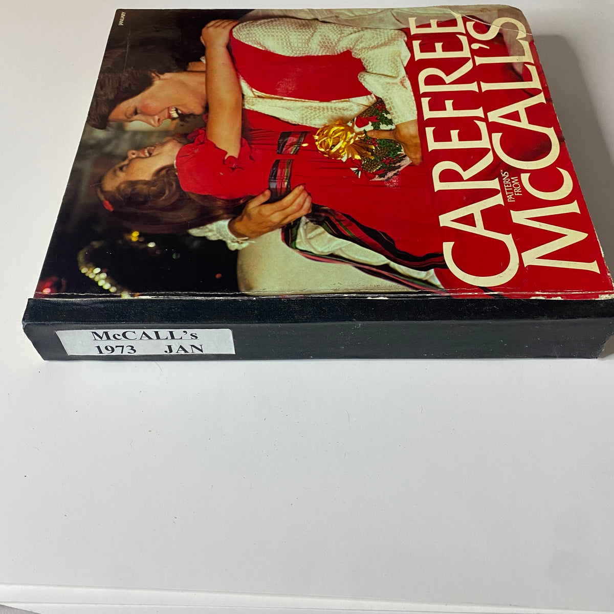Side view of the 1973 January Carefree McCall's Huge Store Retail Counter Catalog with a label, featuring the same joyful mother and daughter from the cover, emphasizing vintage sewing patterns.