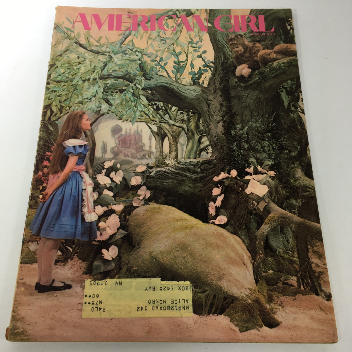 Cover of the VTG American Girl Magazine: January 1973 featuring an illustration of a girl in a blue dress representing Alice from 'Alice In Wonderland' standing in a whimsical garden setting.