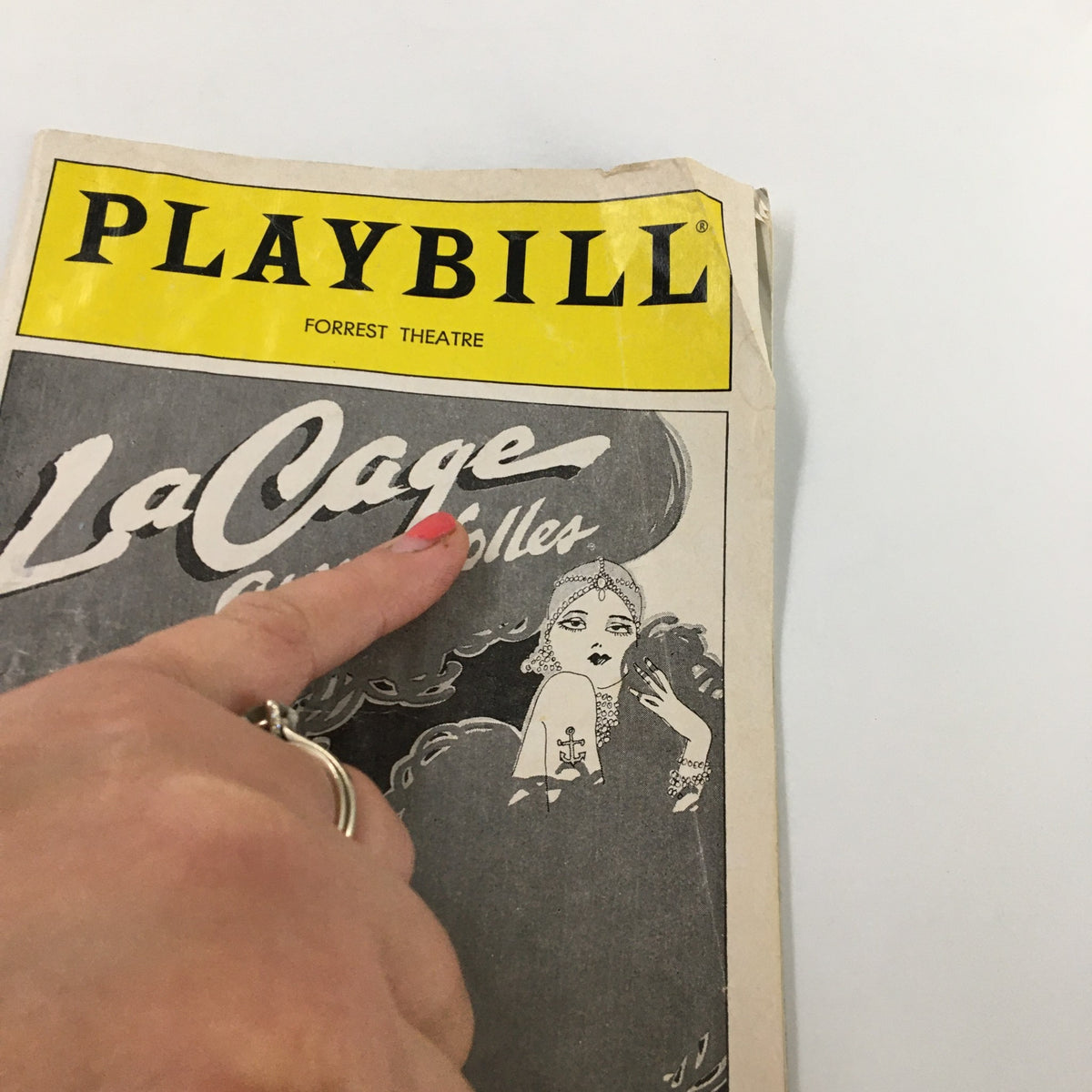 Close-up of the front cover of the 1983 Playbill for La Cage Aux Folles at the Forrest Theatre, featuring a hand pointing at the title.