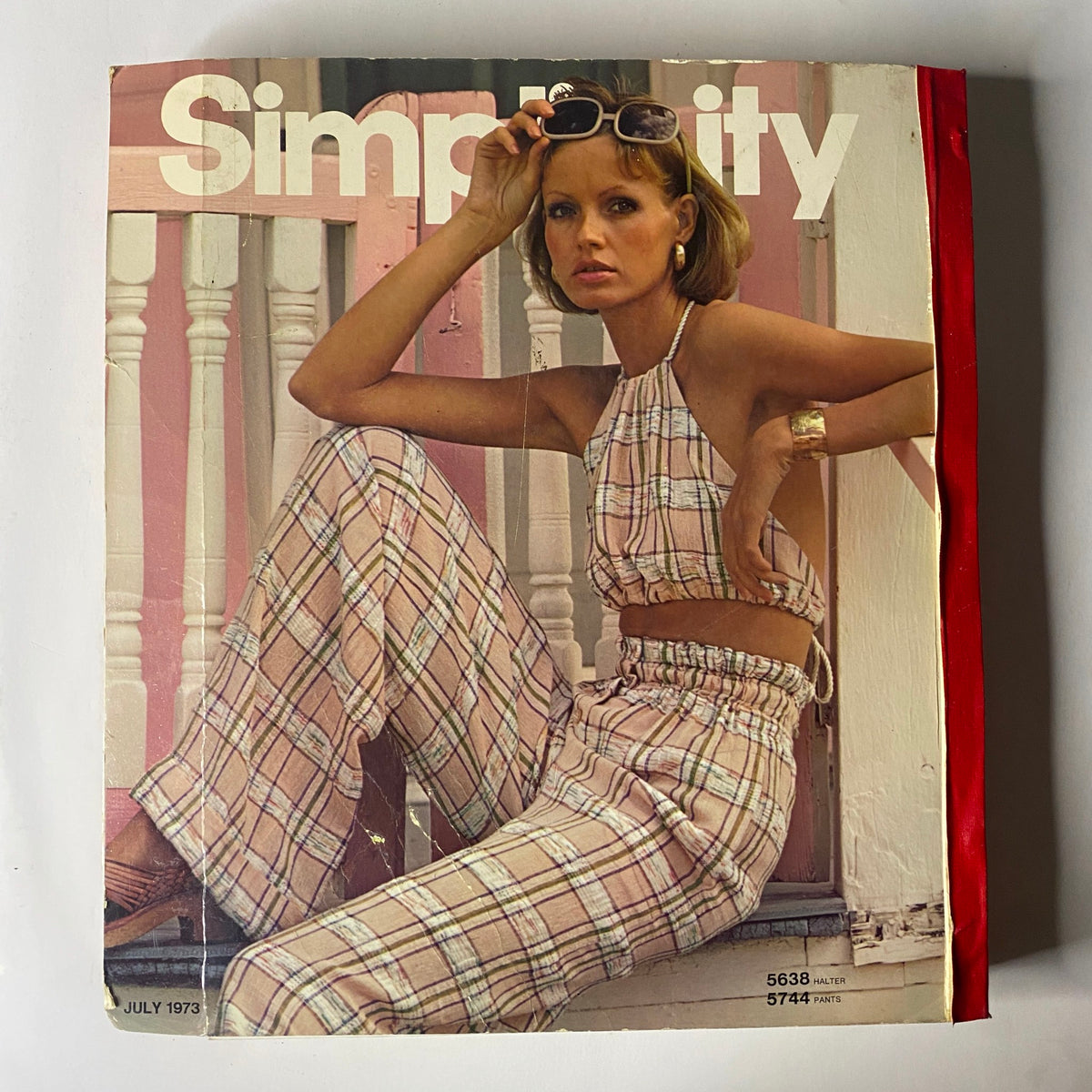Front cover of the 1973 July Simplicity Catalog featuring a model in a plaid two-piece outfit, capturing the summer fashion trends of the 1970s. This catalog offers a variety of sewing patterns for fashionable clothing.