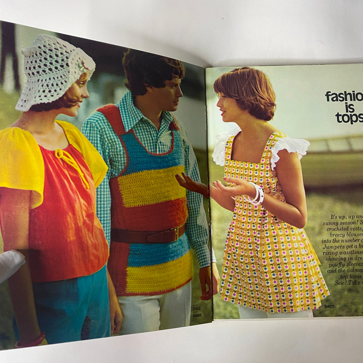 Two models discussing fashion from the 1973 Simplicity Spring Summer School Catalog, featuring vibrant summer styles including a colorful crochet ensemble and a pattern dress.
