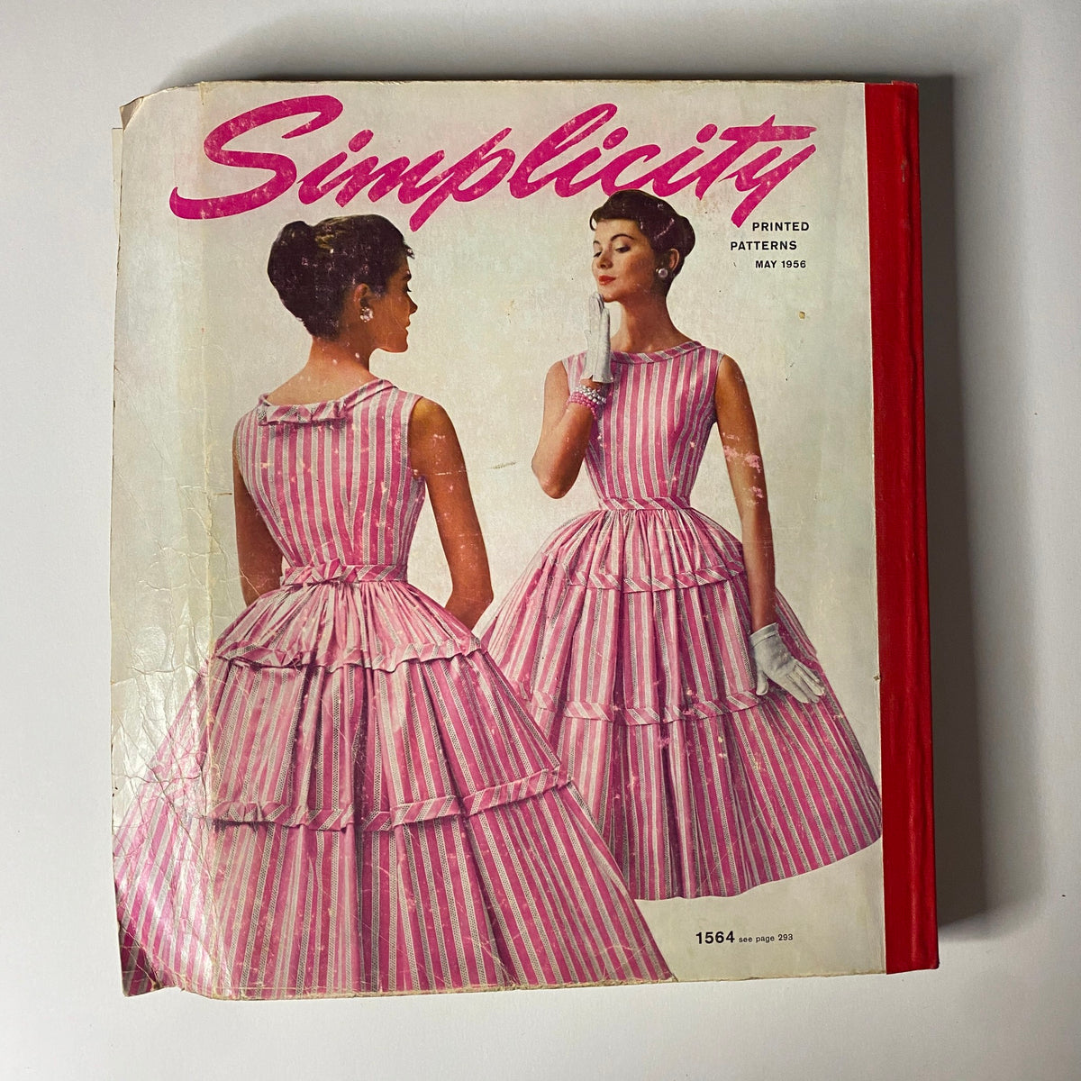 1956 May Simplicity Sewing Pattern Catalog cover featuring stylish models in pink striped dresses, emphasizing mid-century fashion trends and elegance.