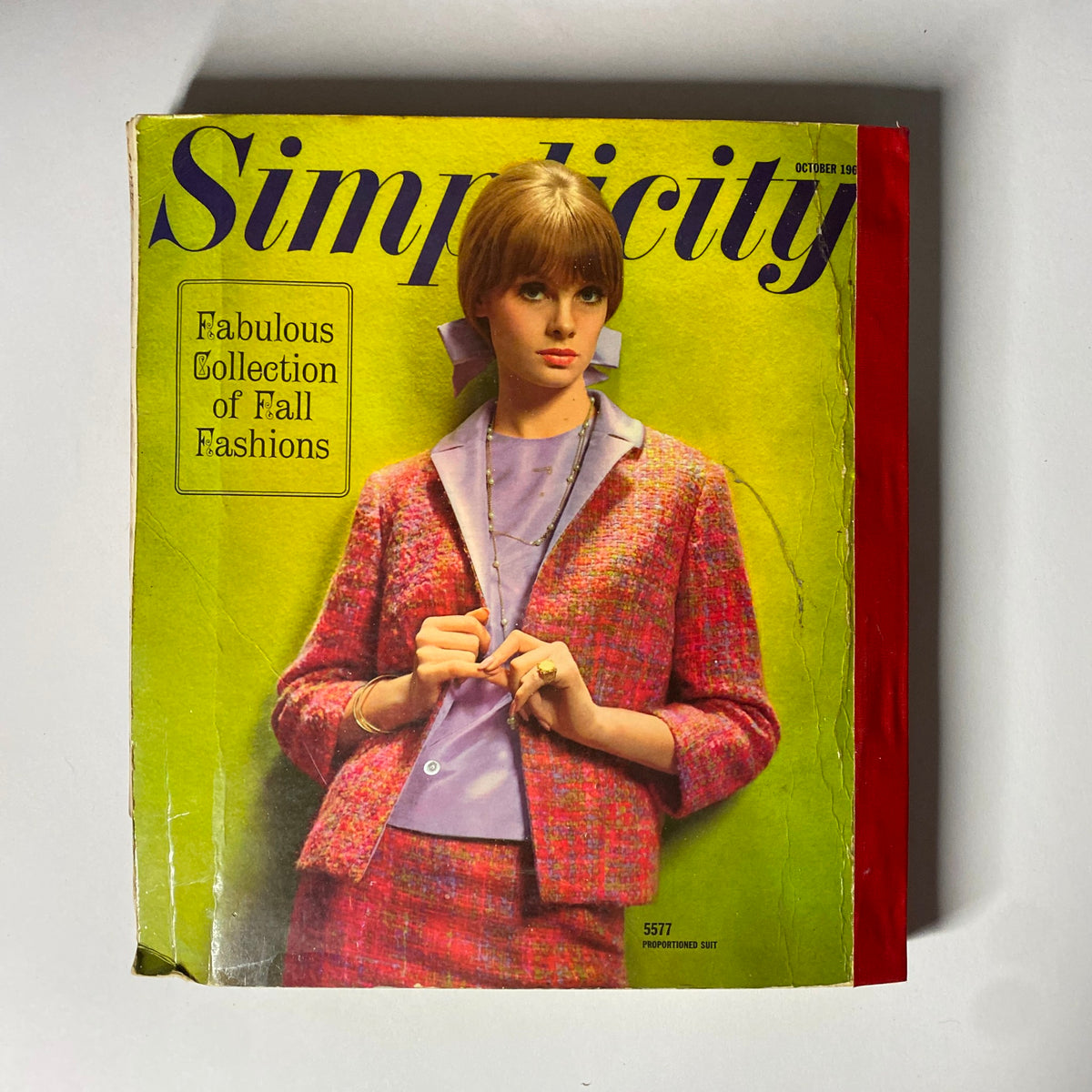 1964 October Simplicity Fall Catalog featuring a model in a vibrant pink and tweed suit, showcasing a collection of fall fashions with a focus on tailored styles and elegance.