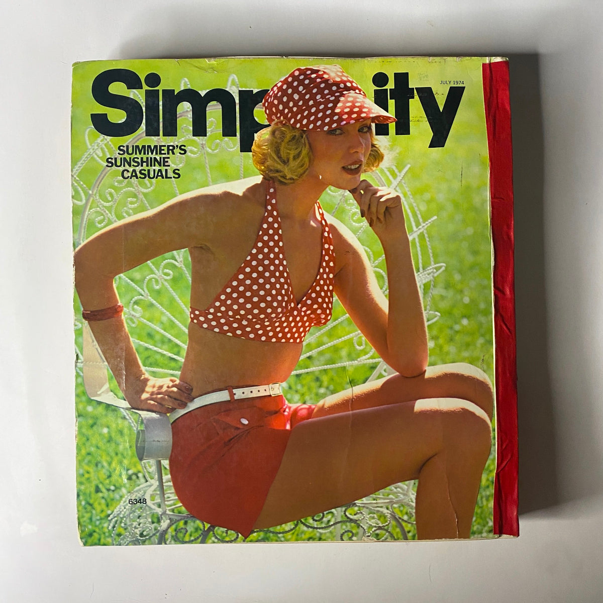 1974 July Simplicity Summer Catalog featuring a model in a polka dot bikini and shorts, promoting summer fashion and sewing patterns.