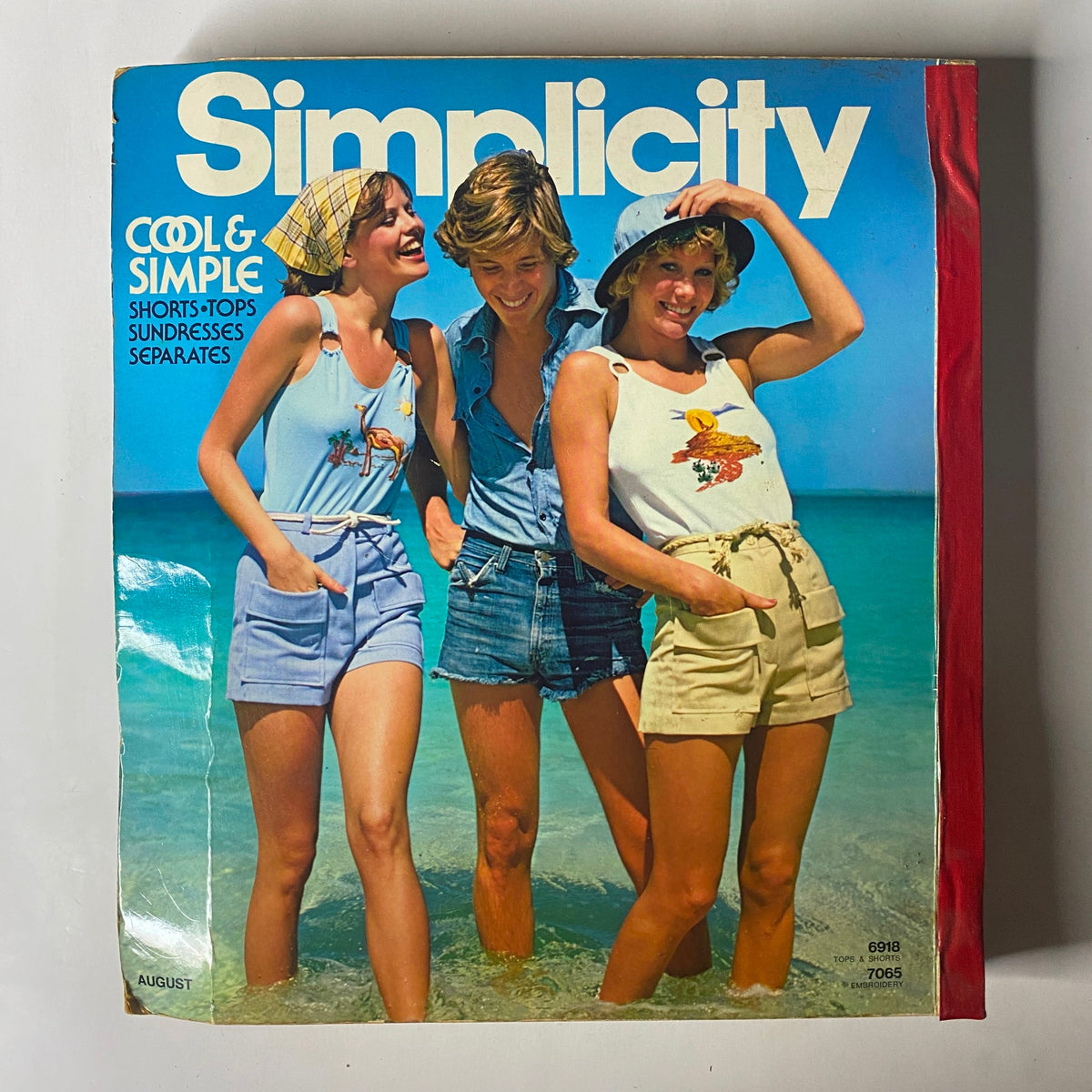 Cover of the 1975 August Simplicity Catalog, highlighting cool and simple summer outfits with models wearing shorts and tank tops on a beach. A great reference for vintage sewing patterns.