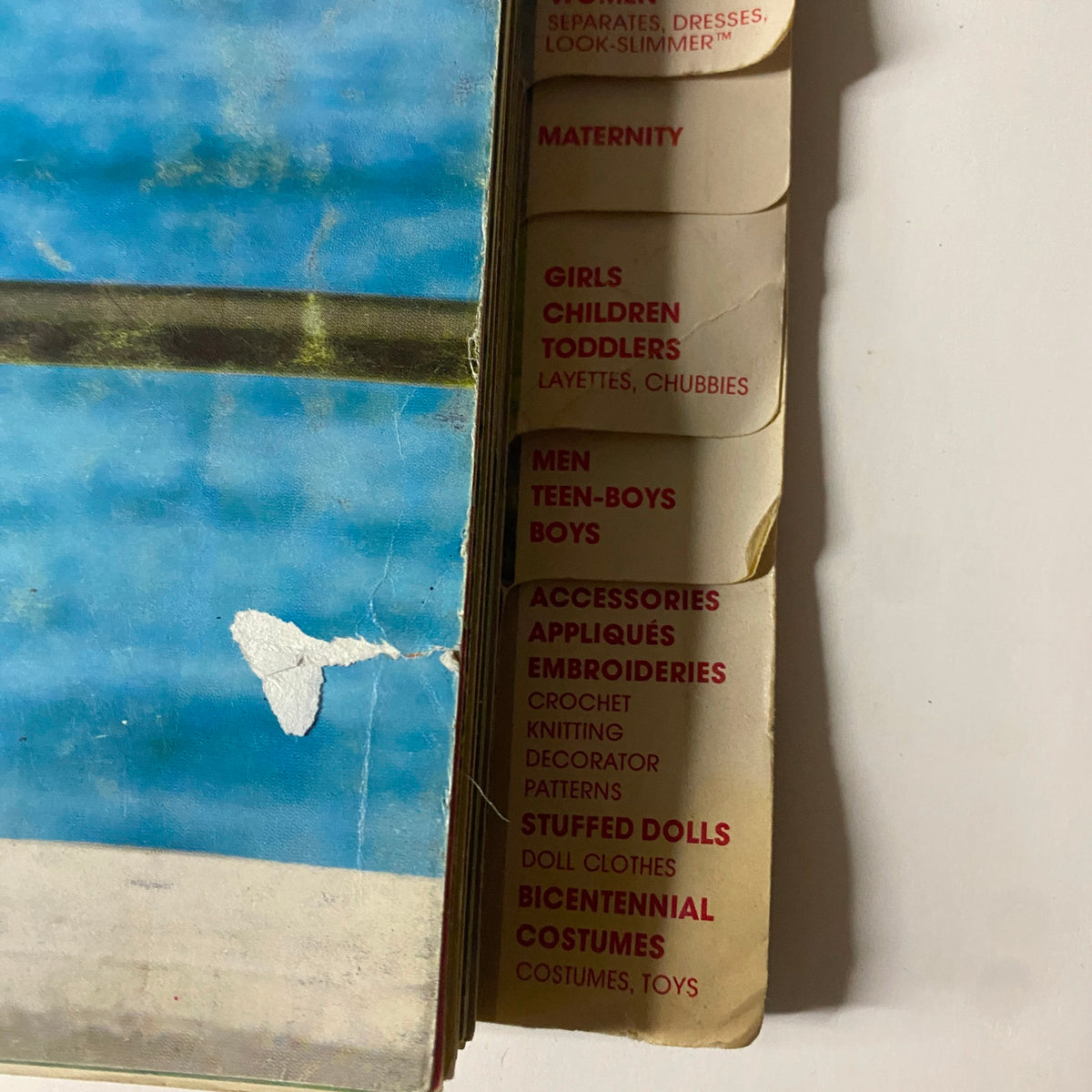Close-up of the spine of the 1976 June Simplicity Catalog, revealing sections like 'Maternity,' 'Girls,' and 'Boys' alongside 'Super Sportswear' tab.
