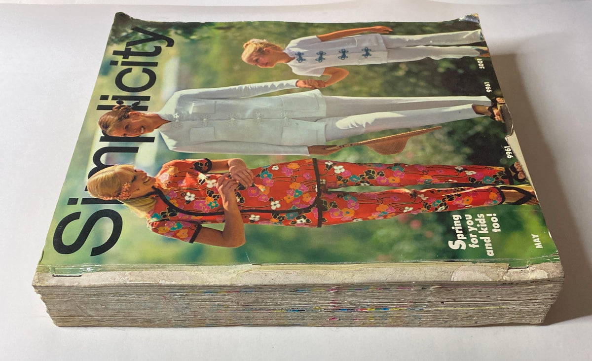 1970s May Simplicity Sewing Pattern Catalog Store Counter Book cover displaying colorful fashion designs for women and children in a sunny outdoor setting.