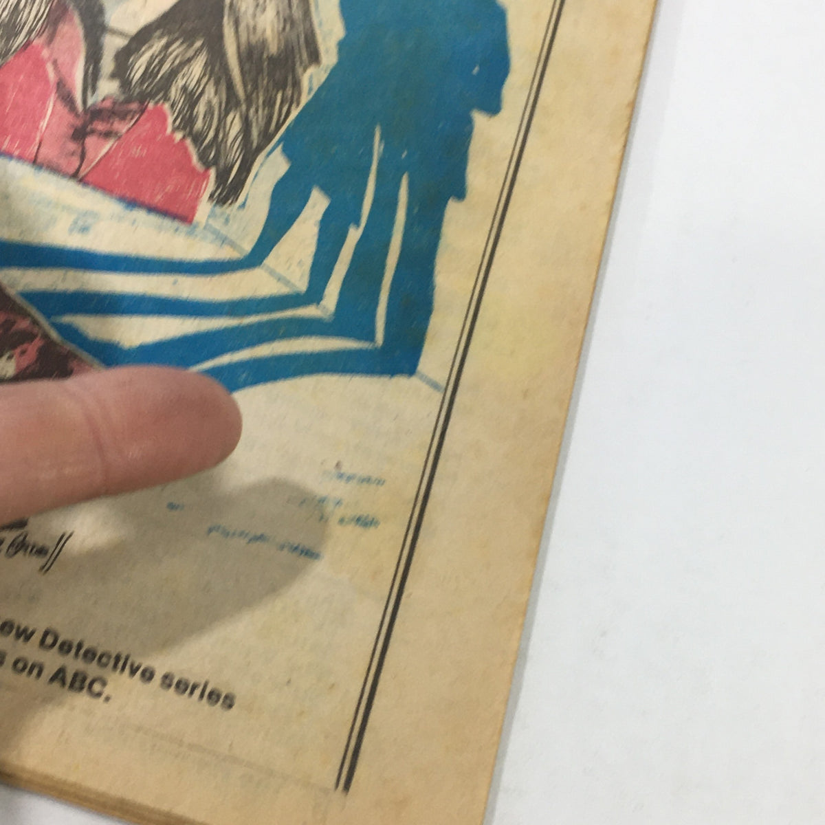 Close-up view of the VTG TV Dial Complete Cable Listings March 26-April 2 1977, highlighting a finger pointing at the detailed illustrated content related to the 'Dog & Cat' series.