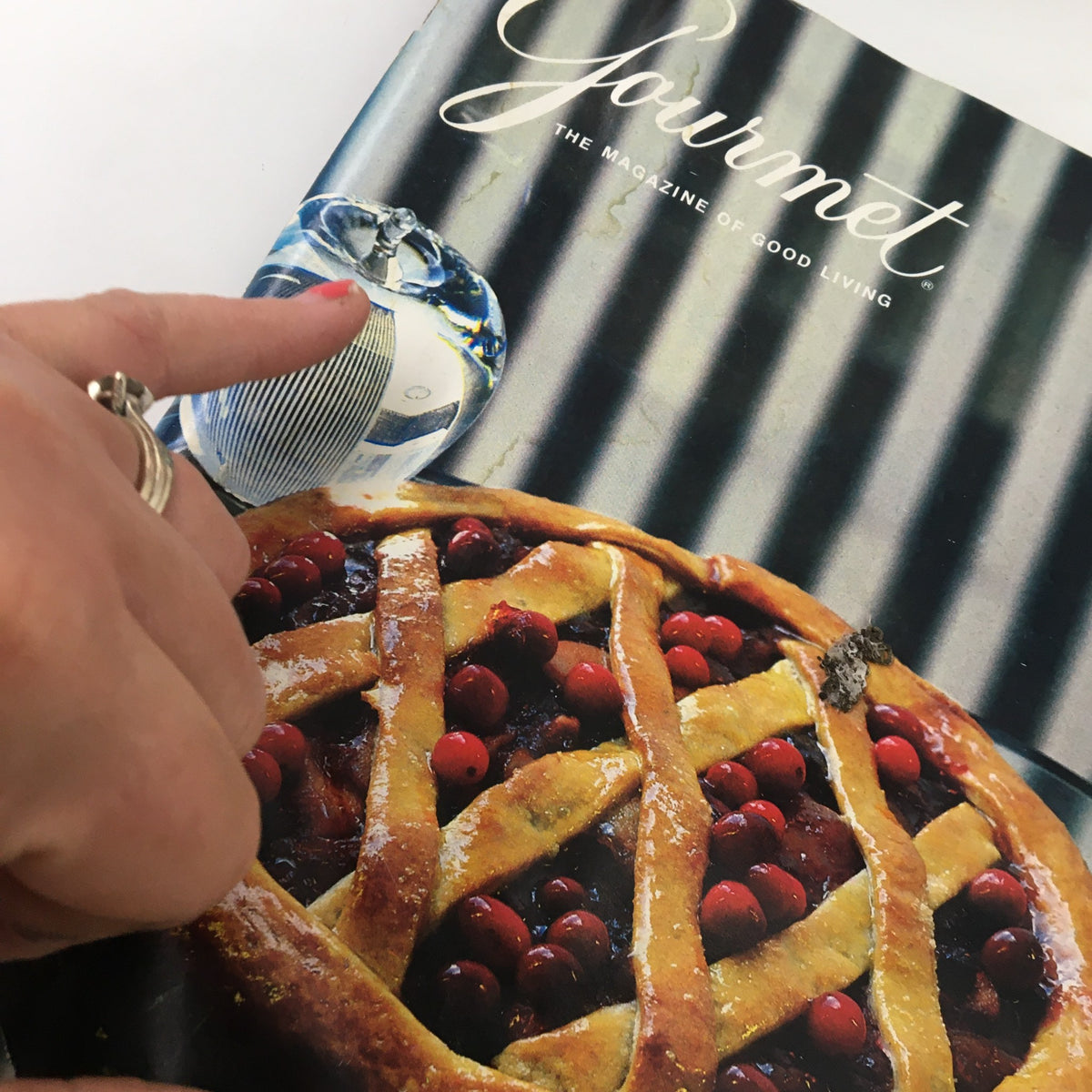 Close-up of the Gourmet Magazine October 1984 cover, highlighting a hand pointing at a decorative glass beside a cranberry pie.