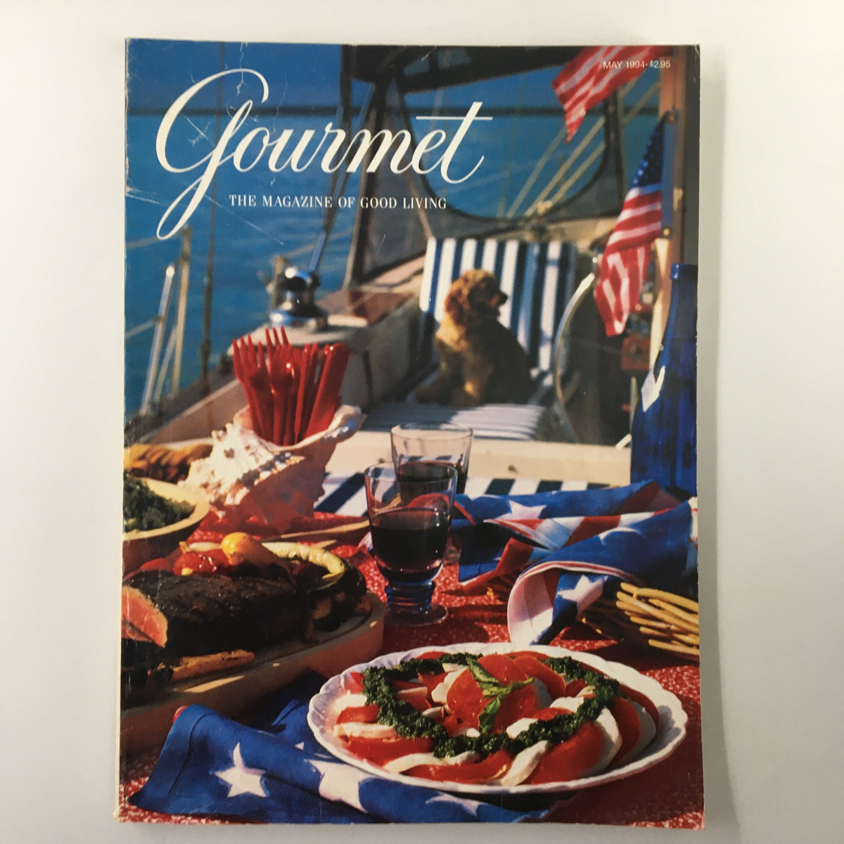 Cover of Gourmet Magazine May 1994 Wine Journal featuring a scenic table setup with food, glasses of red wine, and a dog on a boat, showcasing culinary delights and outdoor dining.