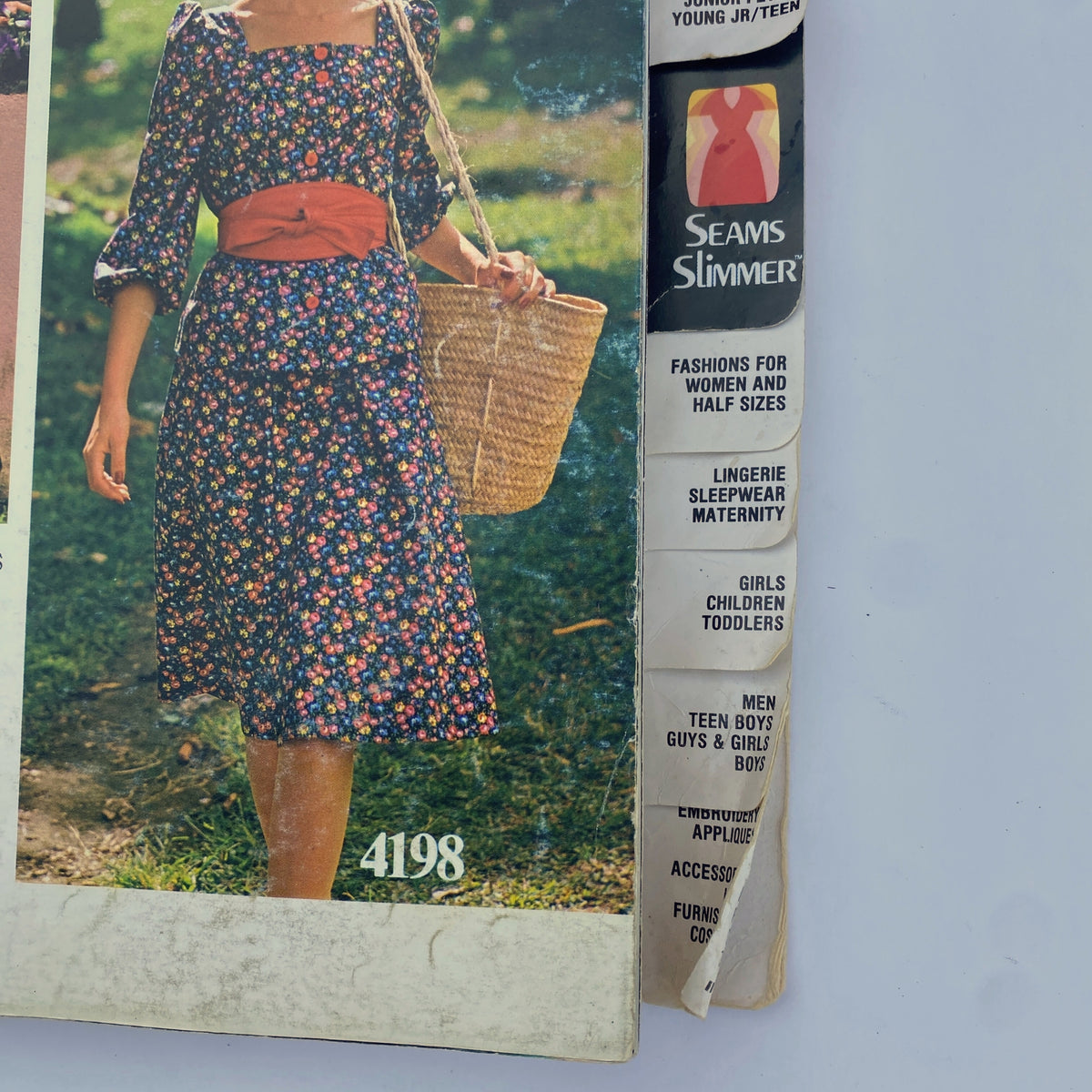 Cover of the 1975 June Butterick Catalog showcasing a floral dress worn by a woman with a straw bag, highlighting vibrant mid-1970s fashion.