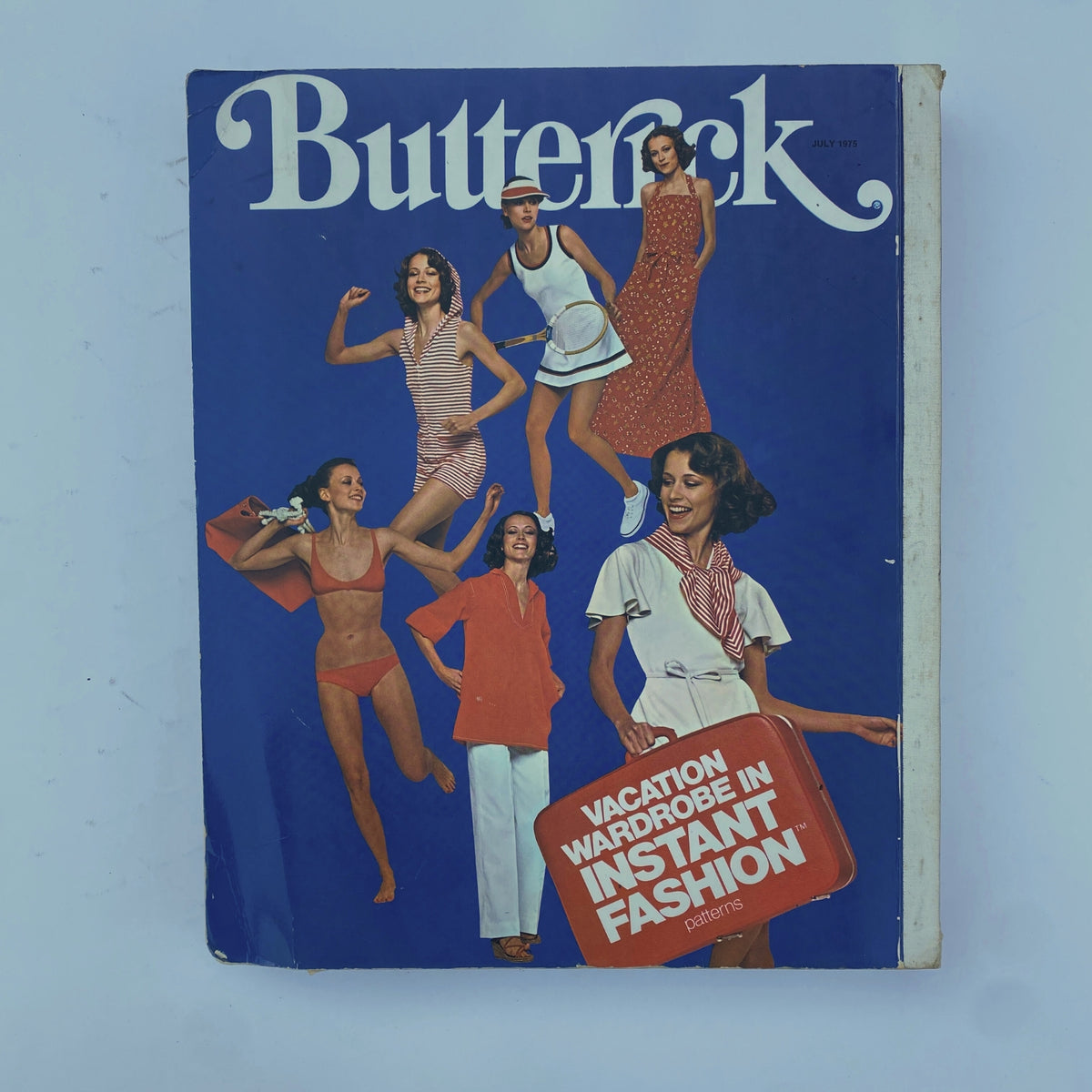 1975 July Butterick Catalog cover displaying vibrant retro fashion patterns, featuring models in stylish summer outfits and the caption 'Vacation Wardrobe in Instant Fashion' highlighting trendy sewing options.