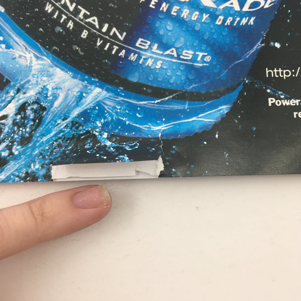 Close-up of a hand pointing at a promotional section for an energy drink on the back cover of Martial Arts Professional Magazine May 2003, illustrating product advertisements.