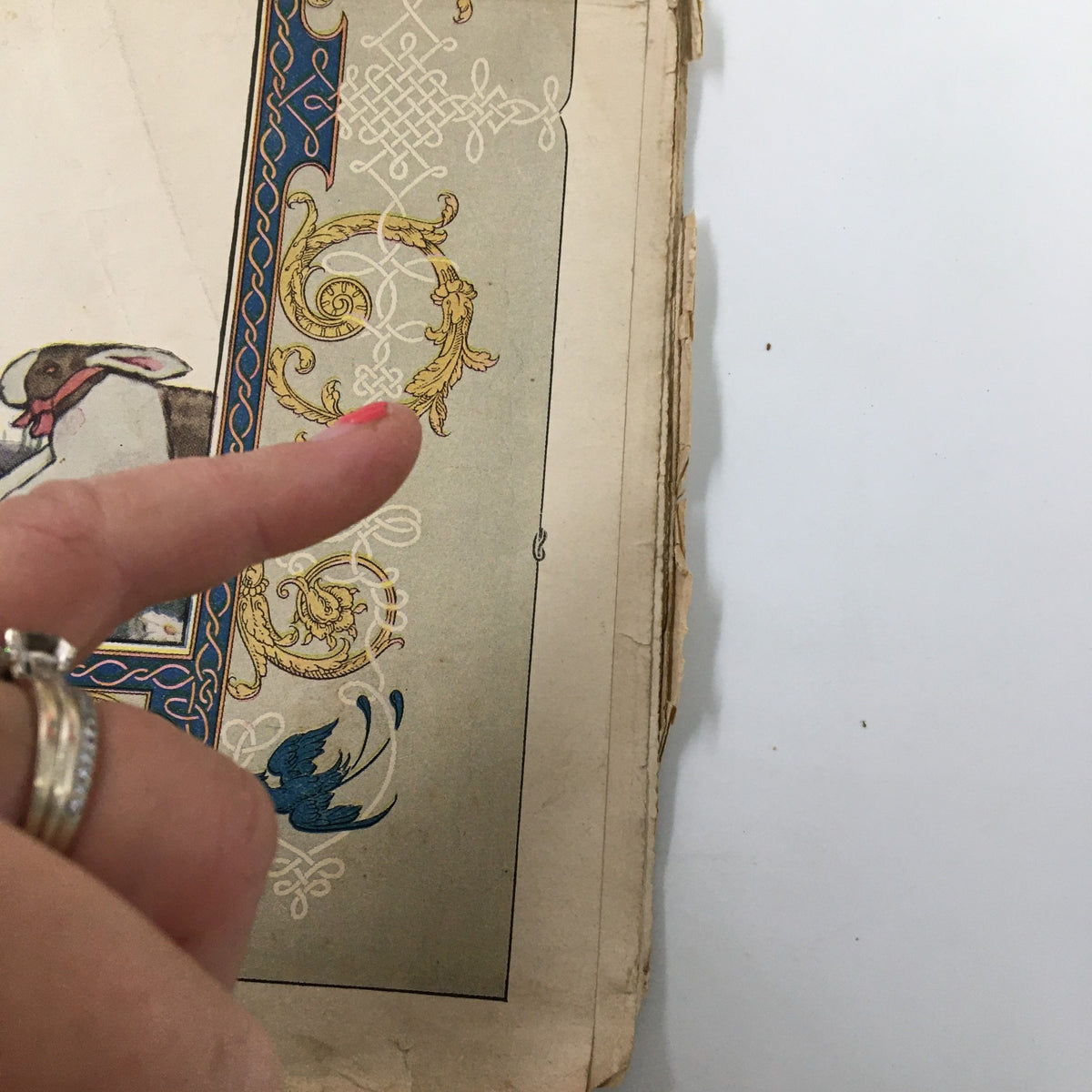 Close-up of the VTG Needlecraft Magazine April 1922 cover featuring intricate decorative elements and a hand pointing to the design.