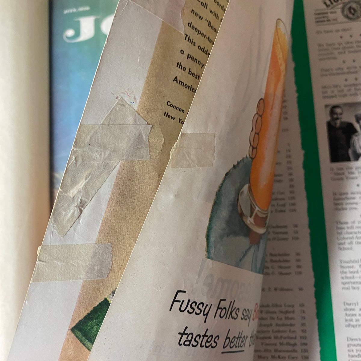Close-up of an advertisement from the Ladies' Home Journal, depicting a hand holding a drink, with vintage tape repair visible on the page.