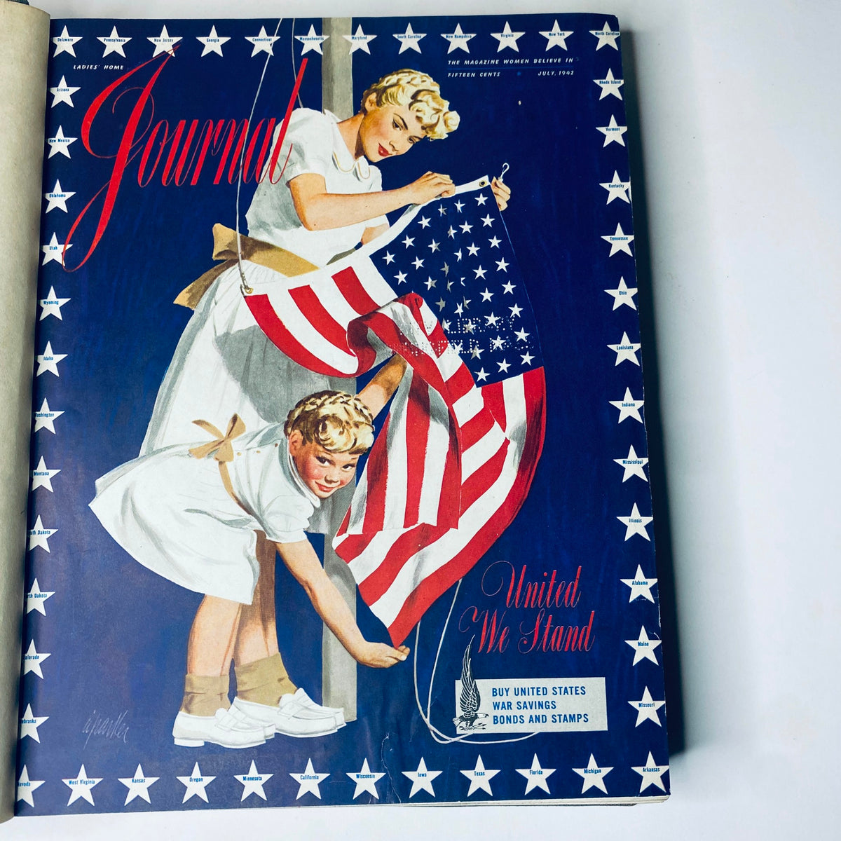 Cover of Ladies' Home Journal Library Bound Magazine 1942, featuring a woman and a child hanging an American flag, reflecting the patriotic spirit of the era during World War II.