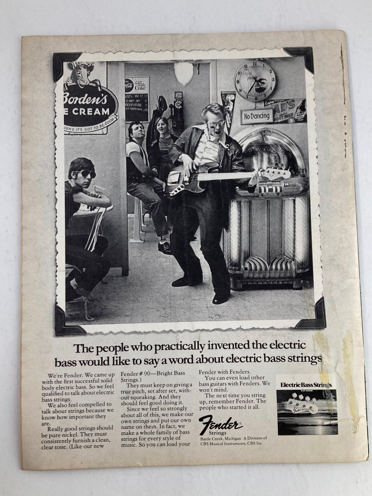 Back cover of Guitar Player Magazine July 1975 displaying an advertisement for Fender Electric Bass Strings, featuring a photograph of musicians in a diner setting, highlighting Fender's legacy in electric bass music.