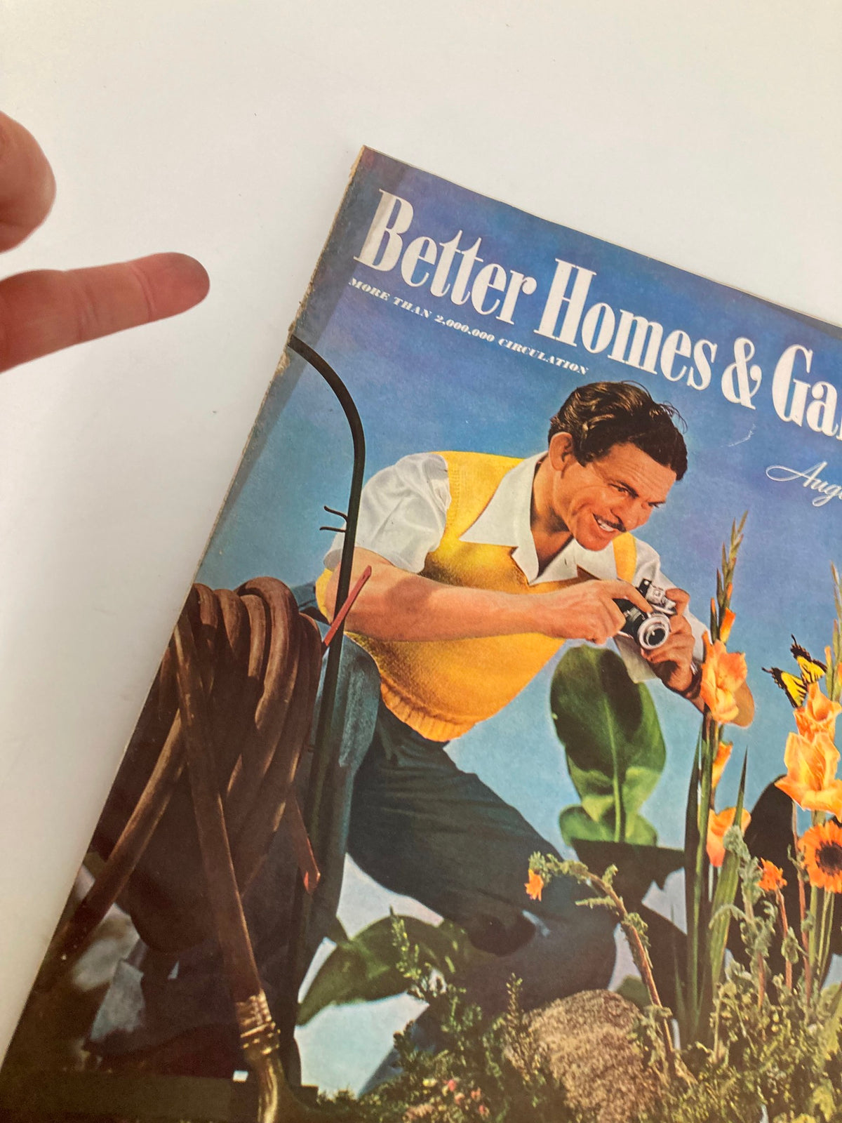 Close-up of the cover of VTG Better Homes & Garden Magazine August 1940 featuring a man taking a photo and vibrant flowers.