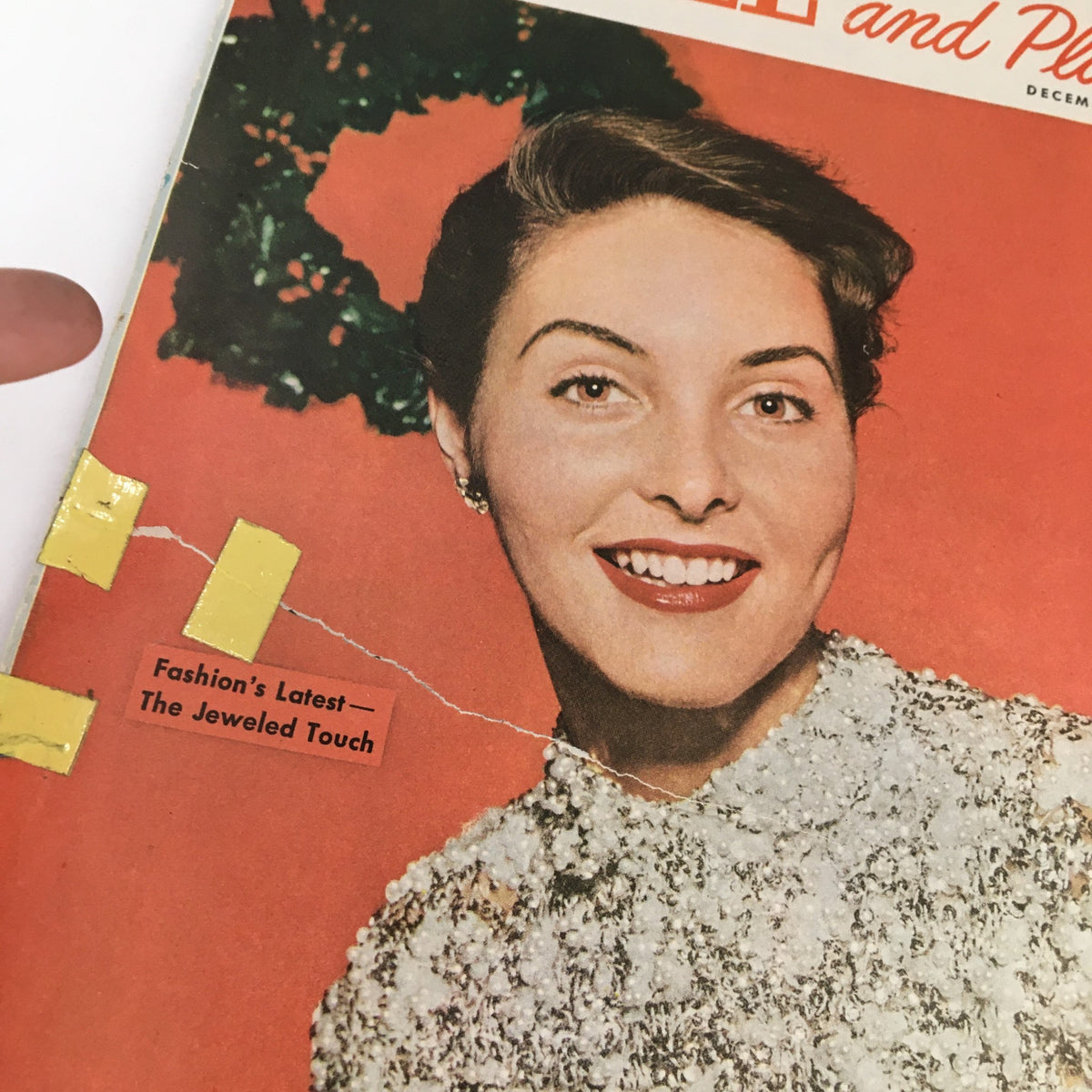 Close-up of the cover of People and Places Magazine December 1952 titled 'Fashion's Latest: The Jeweled Touch', highlighting a smiling woman adorned in a stylish outfit with decorative elements, representing the fashion trends of the early 1950s.