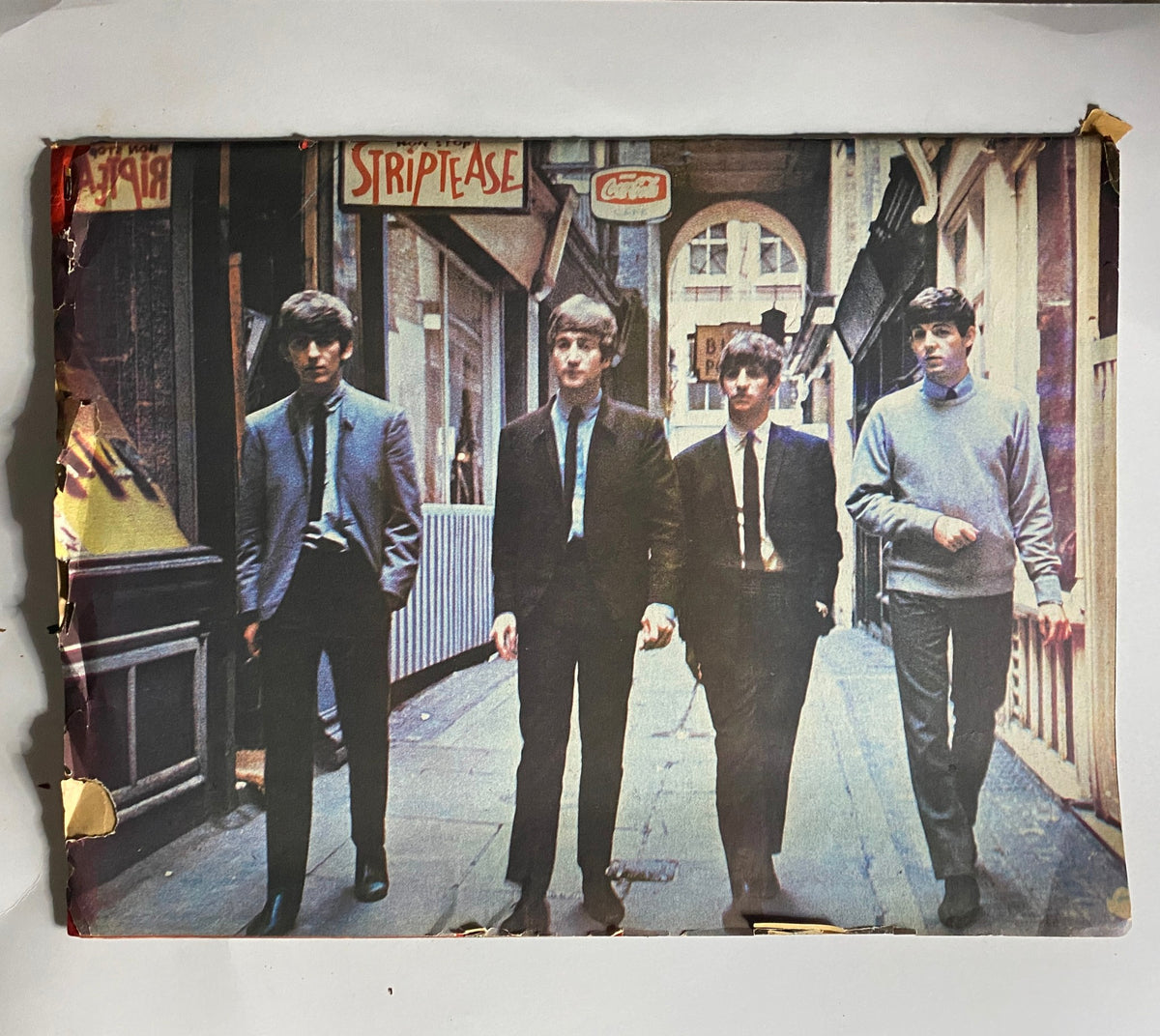 The Beatles walking down a street in 1964, captured in a vintage magazine, reflecting the iconic fashion and style of the era, an essential component of the Beatlemania collectors item.