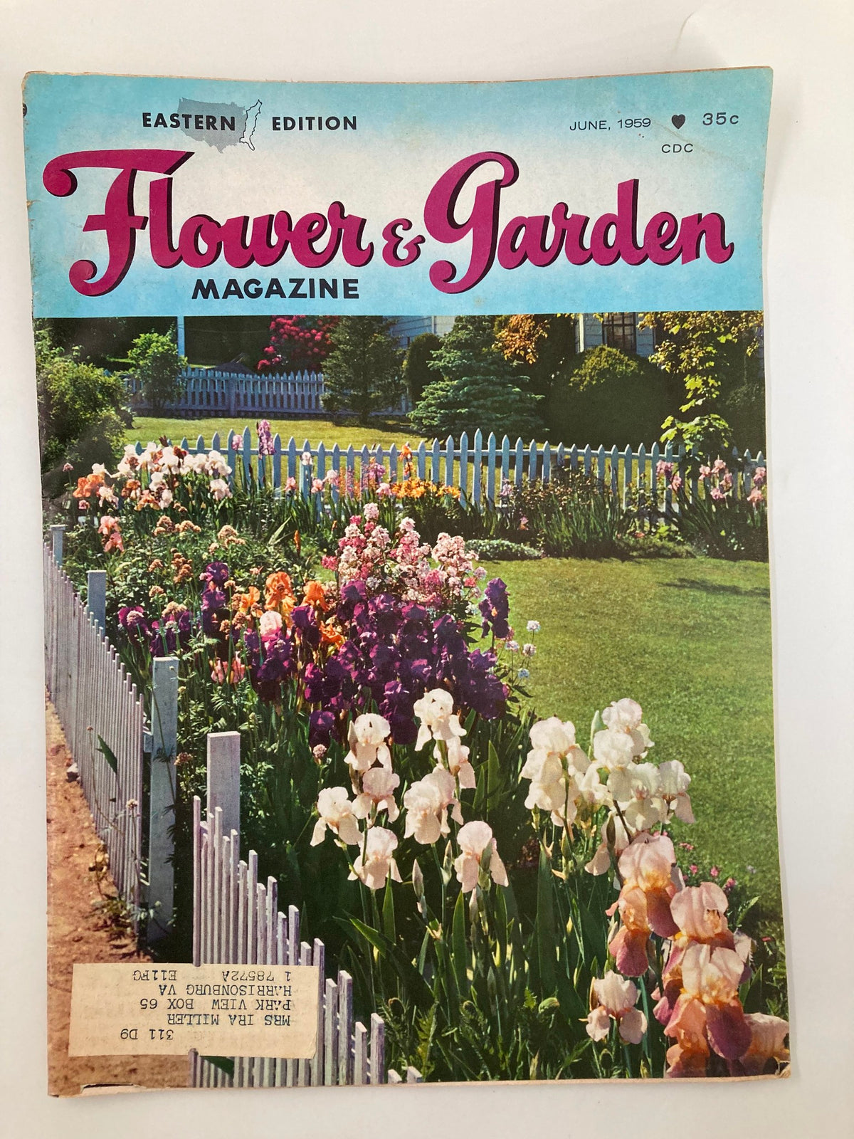 Cover of the VTG Flower and Garden Magazine June 1959 featuring a vibrant garden with blooming irises and a white picket fence, showcasing gardening charm and nostalgia.