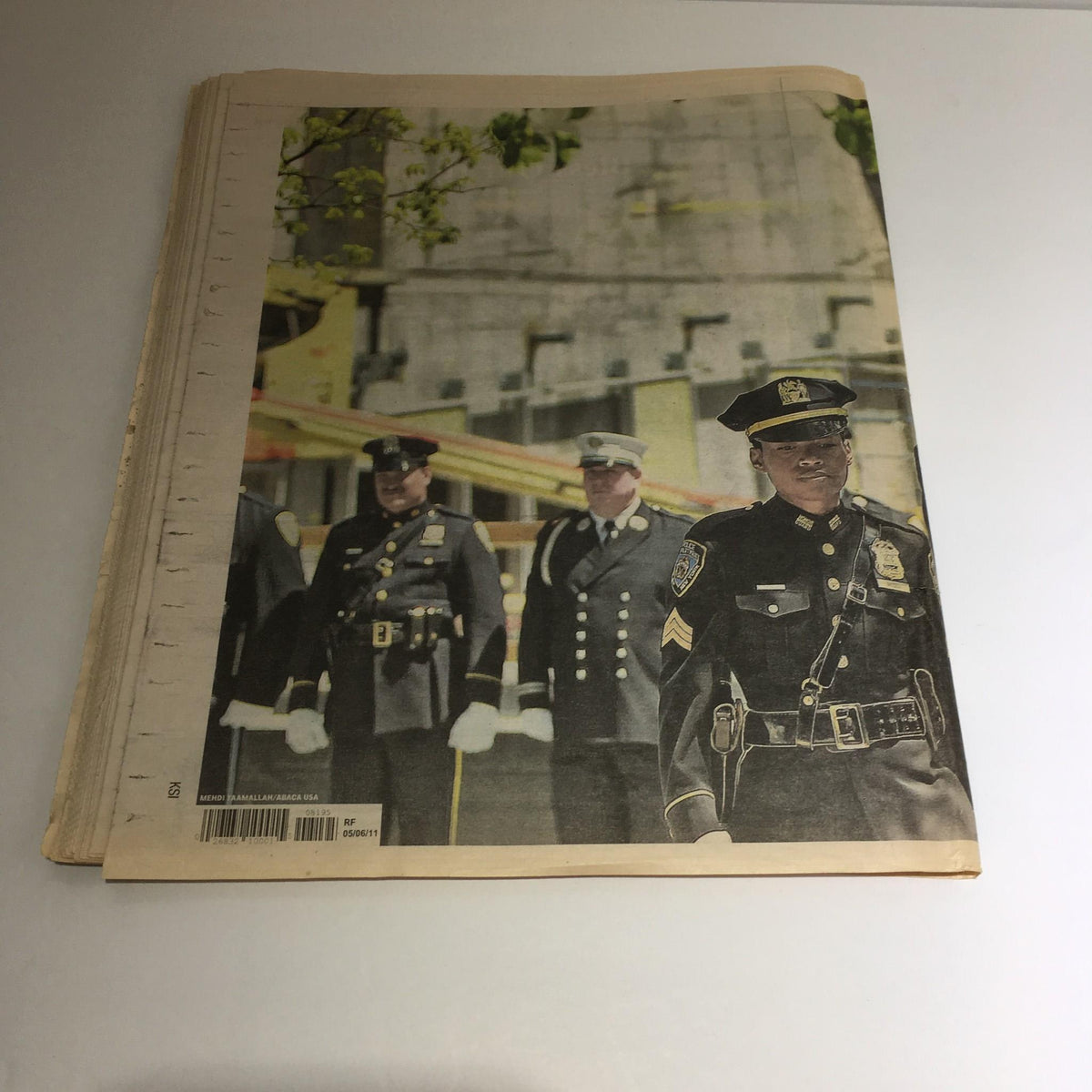 Back cover of the NY Daily News from May 6, 2011, depicting a police officer in uniform, emphasizing the memorial aspect of Obama's visit to Ground Zero, with 'We'll Never Forget' text.